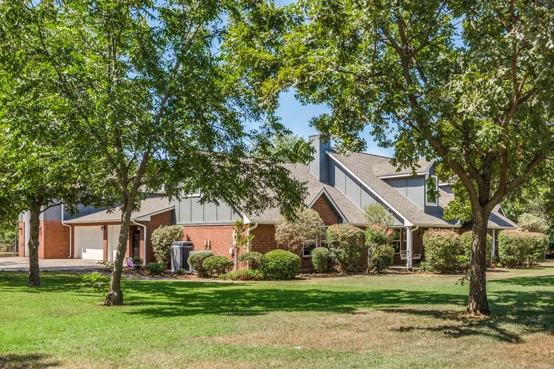 Brick and siding exterior, multi-pitch roofline, front porch, mature trees, and an attached two-car garage