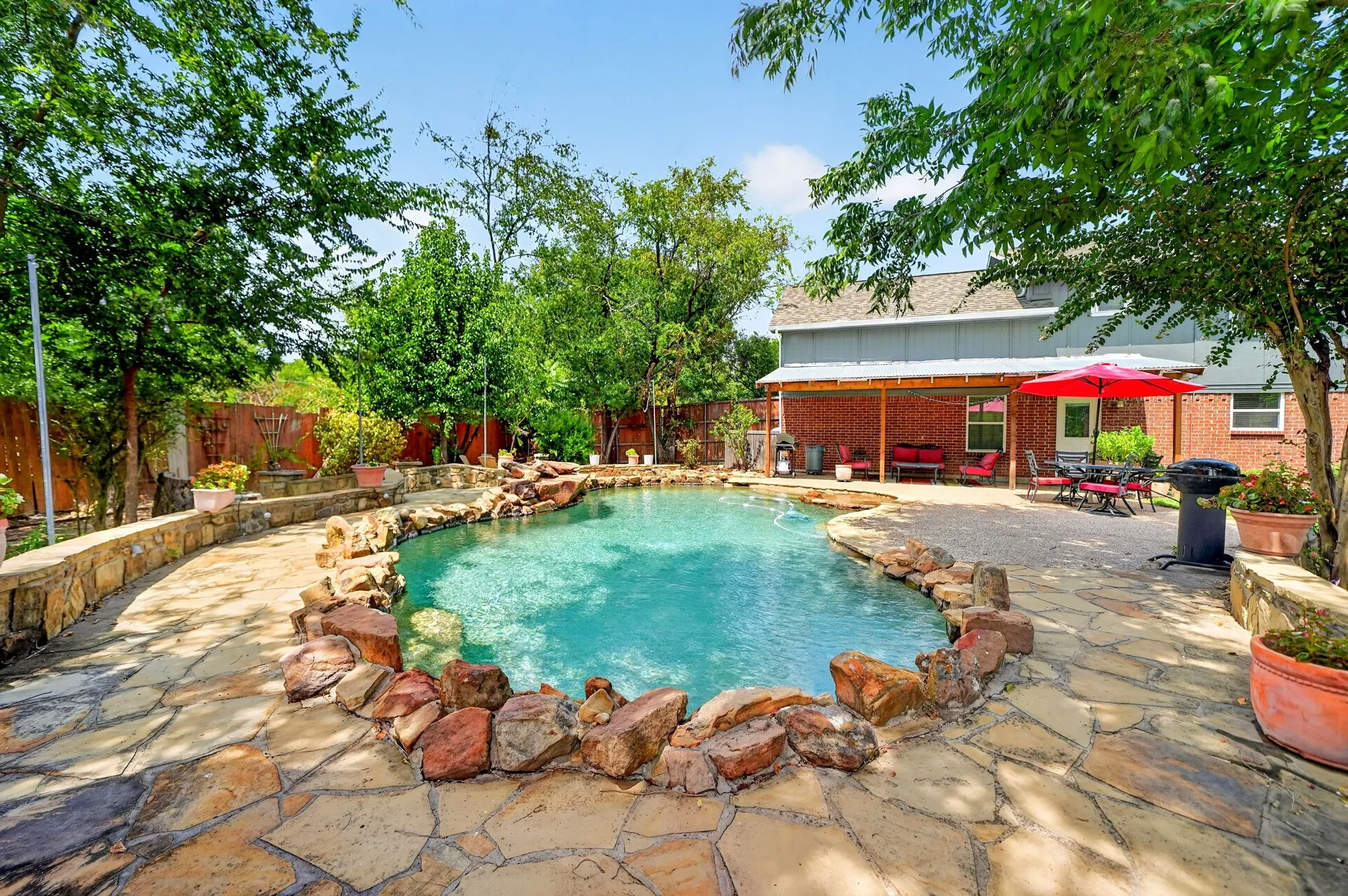 Freeform pool with rock coping, flagstone patio, stone retaining wall, and covered porch with brick columns