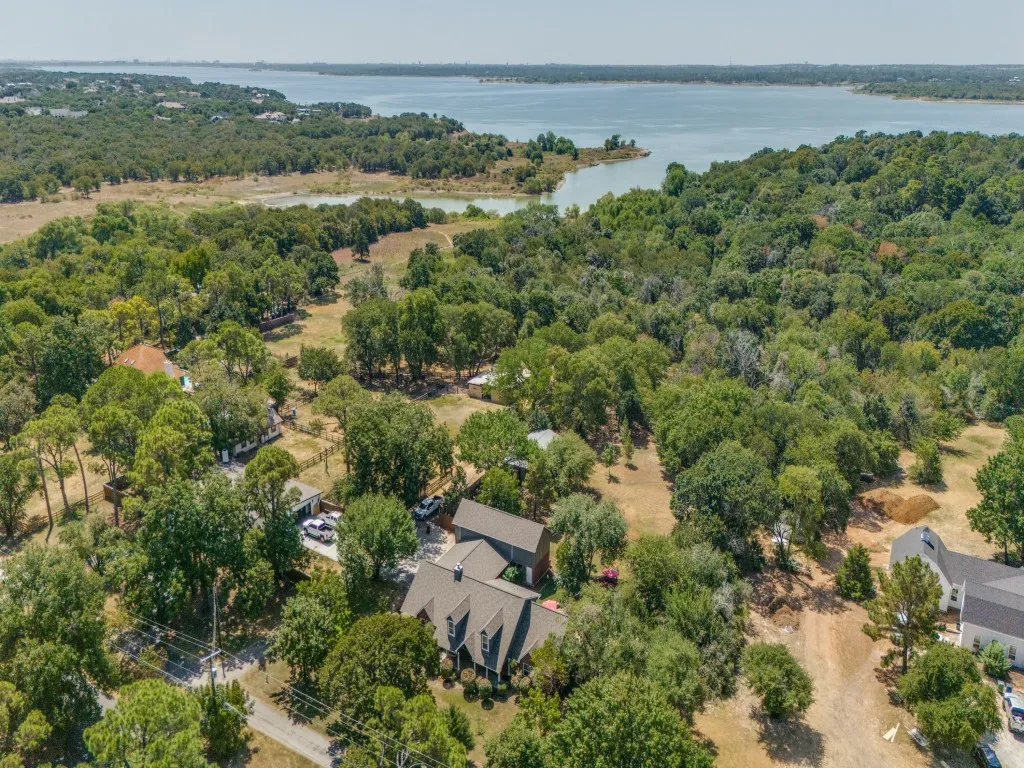 Expansive property situated within a lush, wooded landscape, featuring a prominent body of water in the background