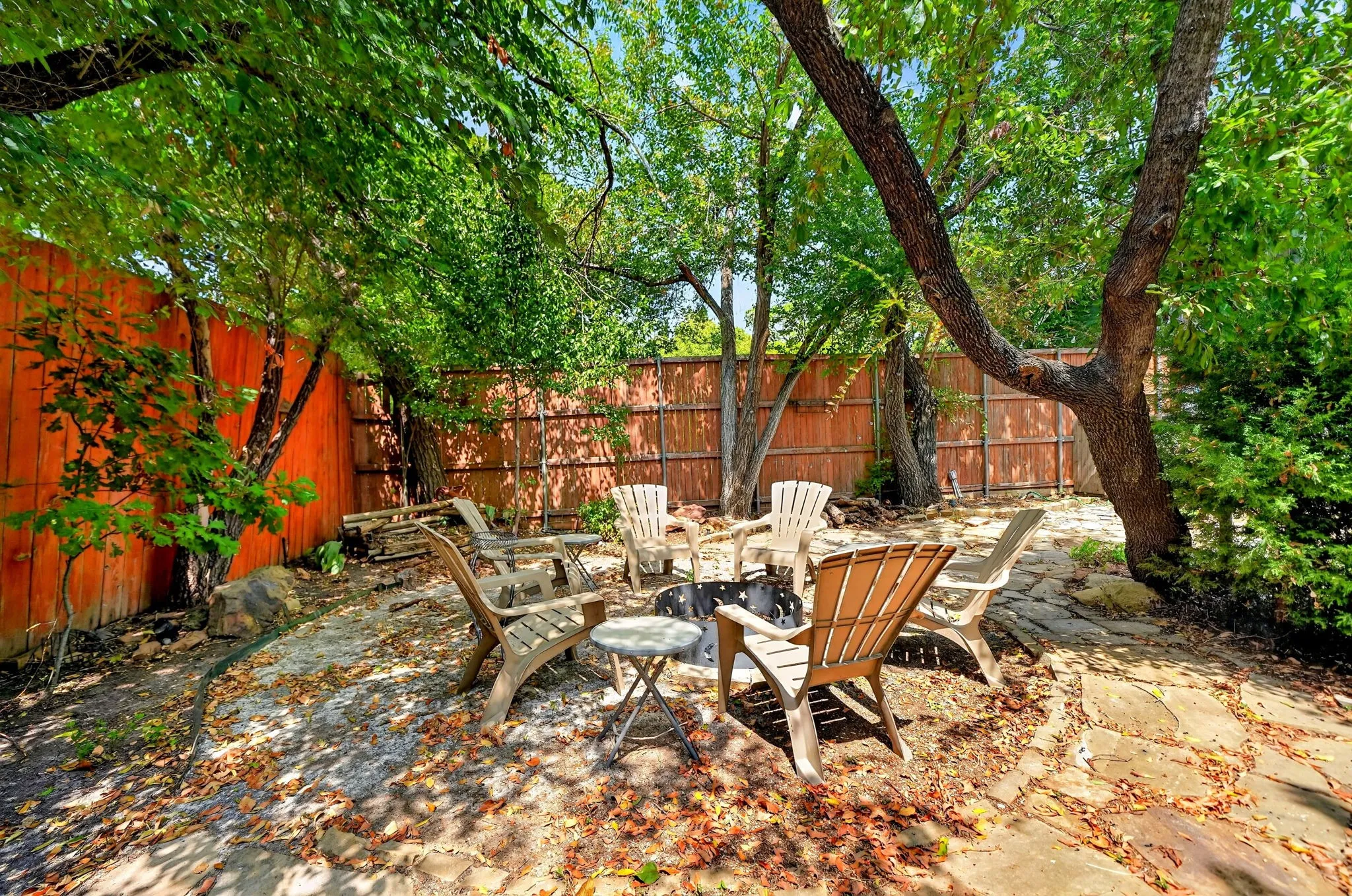 Private backyard with flagstone paving and mature trees, enclosed by a wood privacy fence