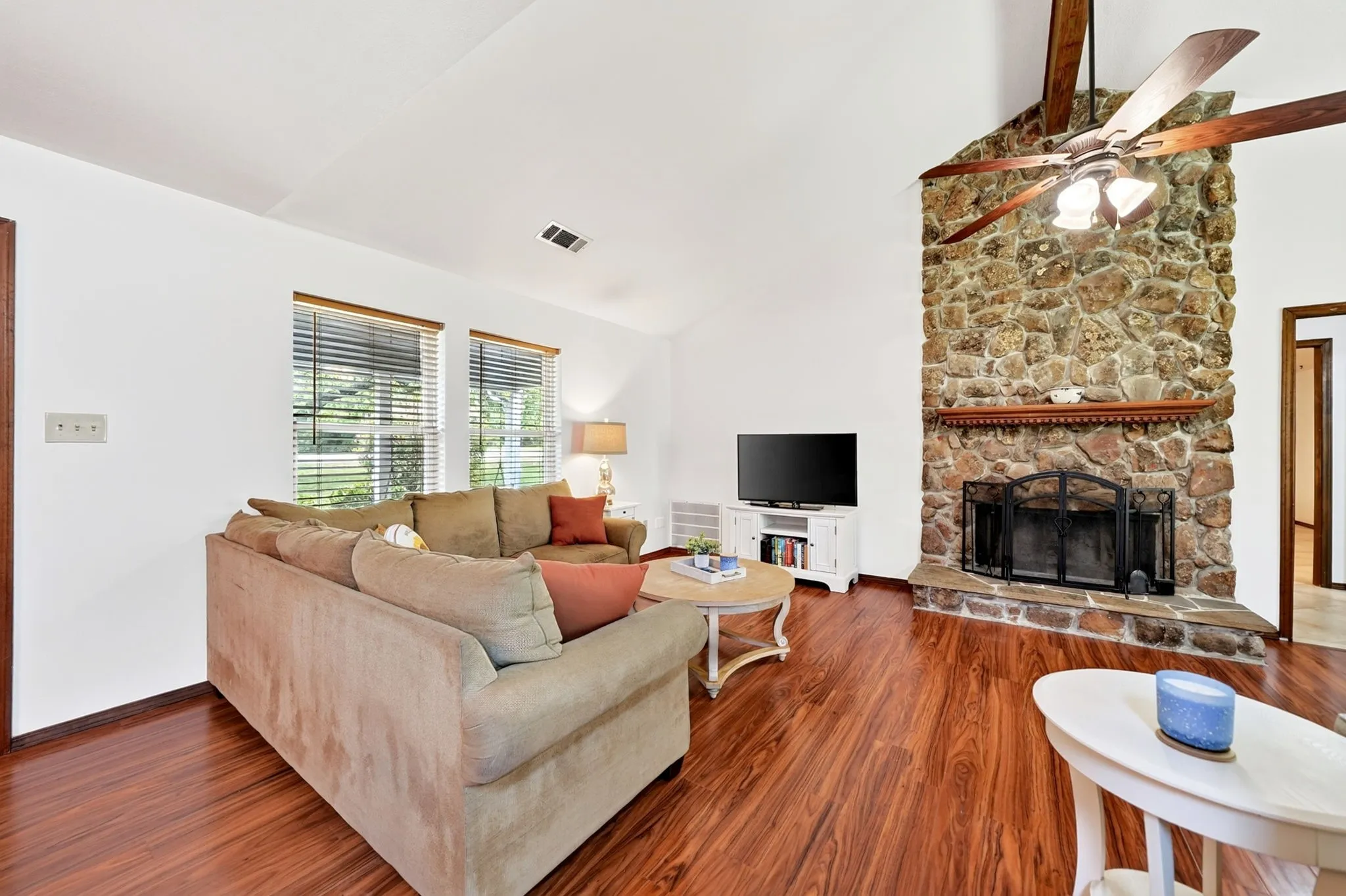 Vaulted ceiling with exposed wood beams, stone fireplace, wood-finish flooring, and recessed lighting