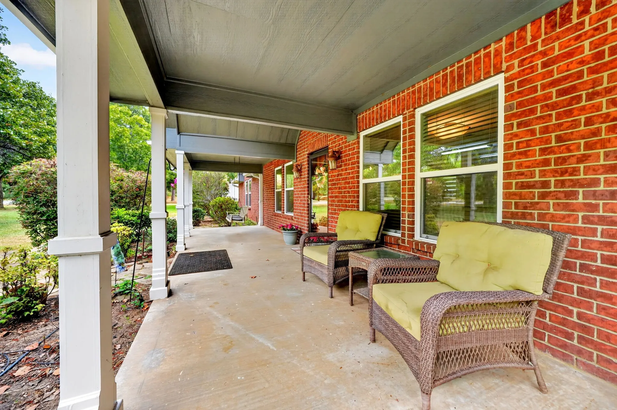 Covered front porch with concrete flooring, brick exterior, and multiple windows