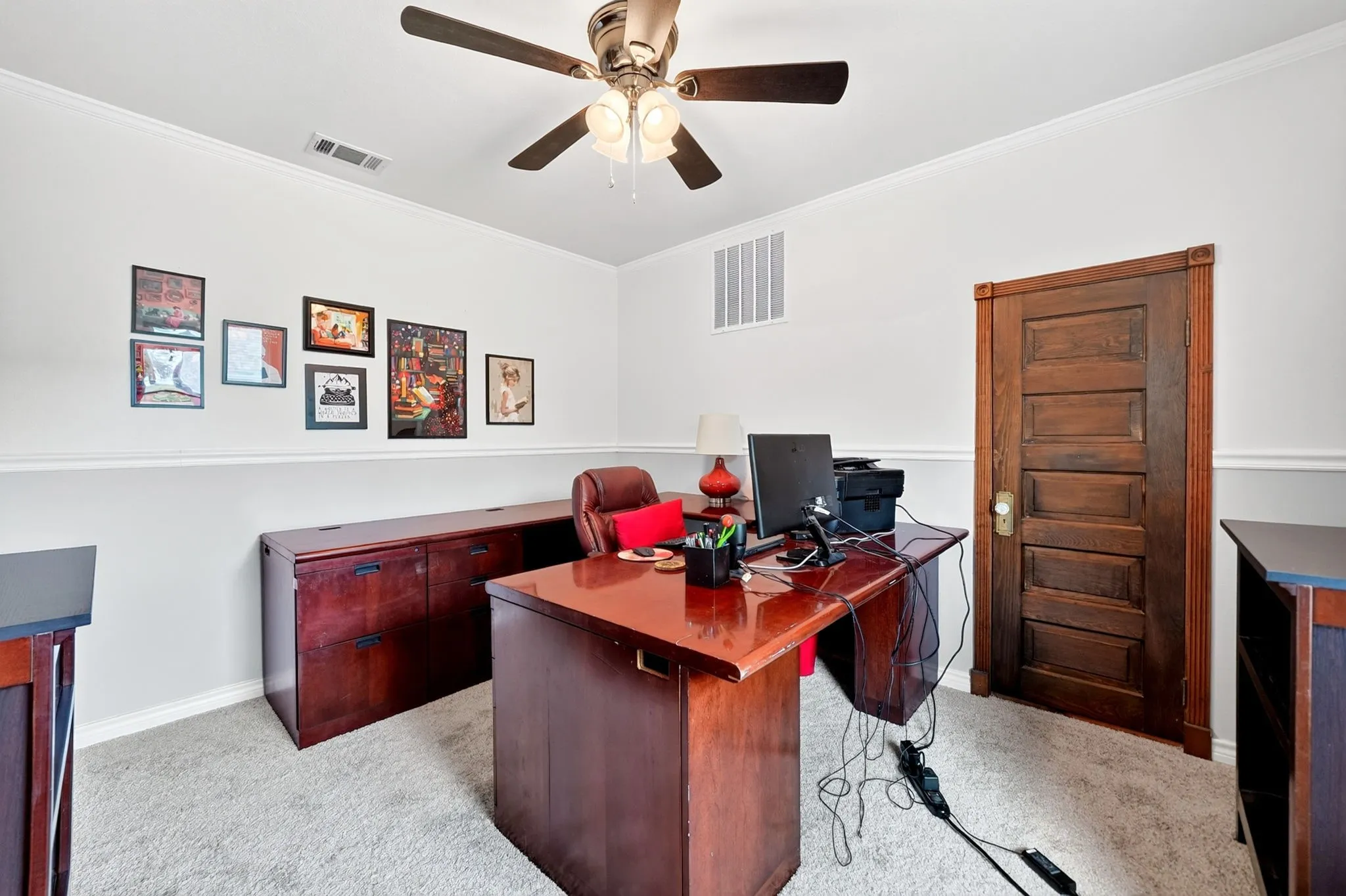 Crown molding, two-tone wall treatment, ceiling fan with integrated lighting, wood-finish panel door, and plush carpet flooring