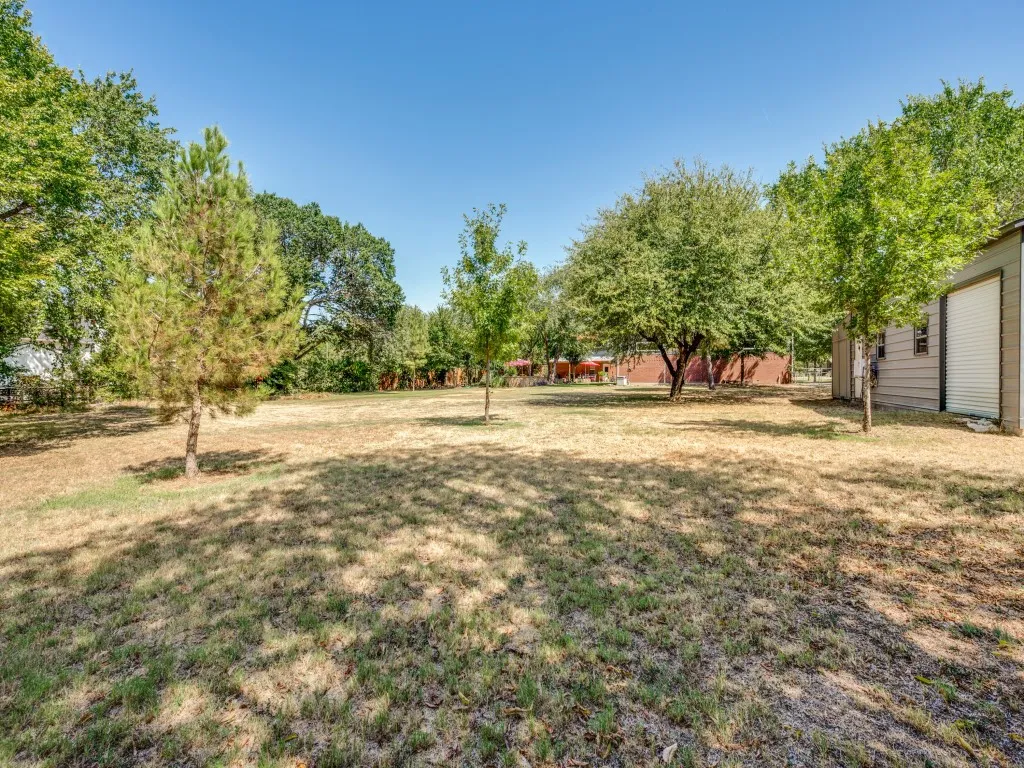 Expansive outdoor space featuring a detached storage shed, mature trees, and a clear sky