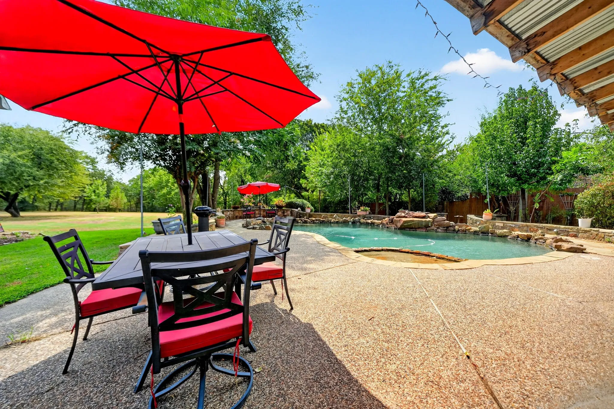 Expansive outdoor living area featuring a swimming pool, stone accents, concrete decking, and mature landscaping