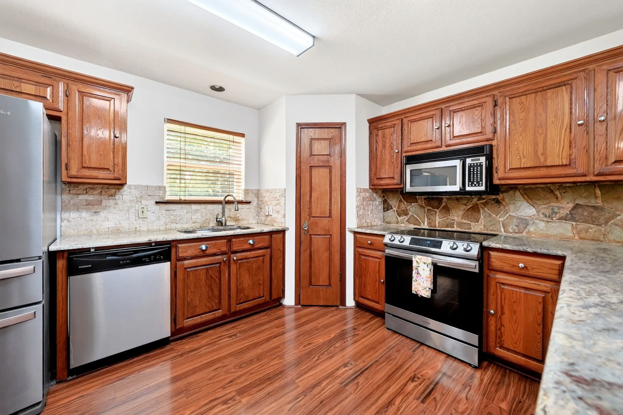 Wood-finish flooring, wood cabinetry, stone countertops, stainless steel appliances, and a stone backsplash