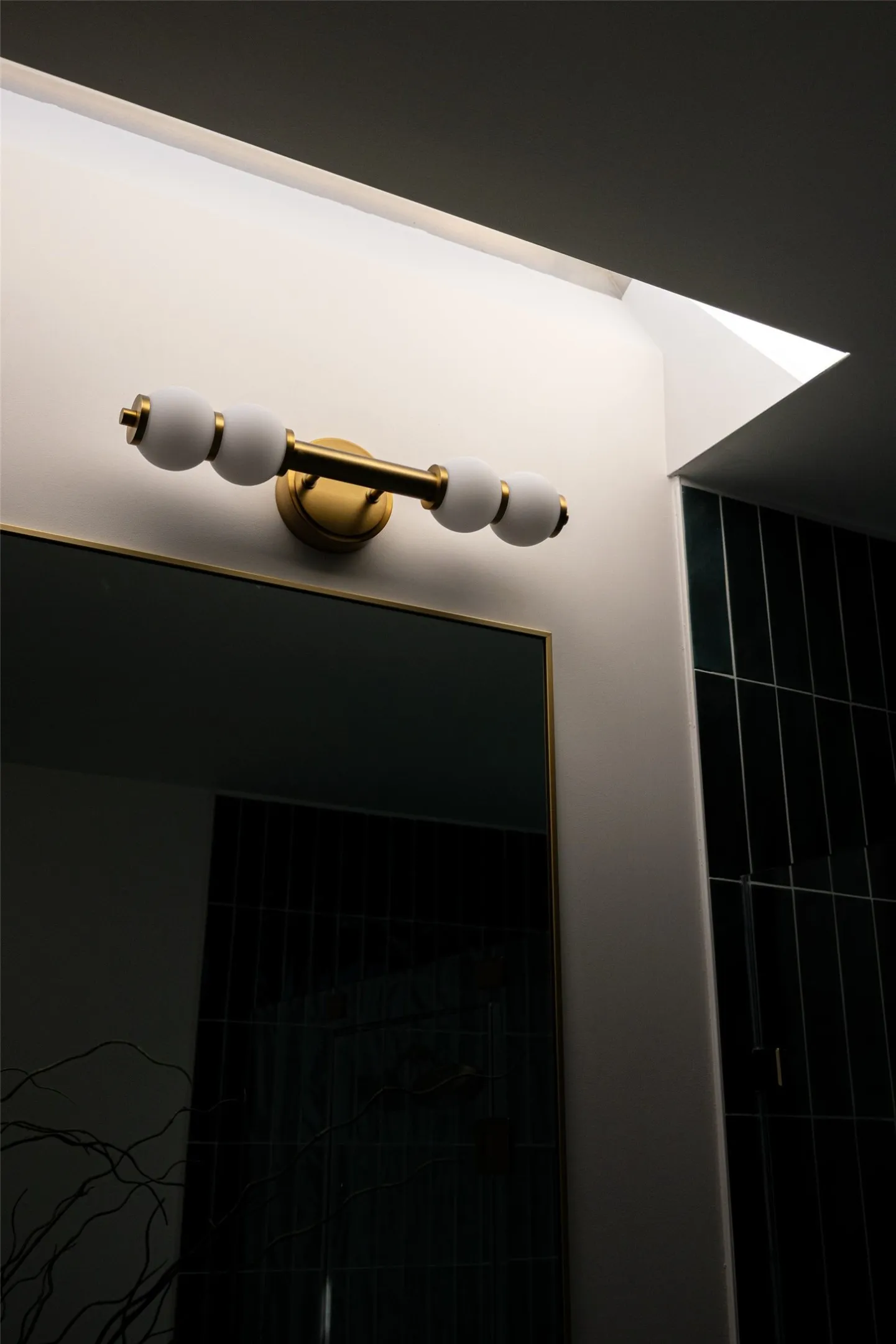 Gold-tone vanity light fixture with frosted spherical shades, framed mirror, and dark tiled wall