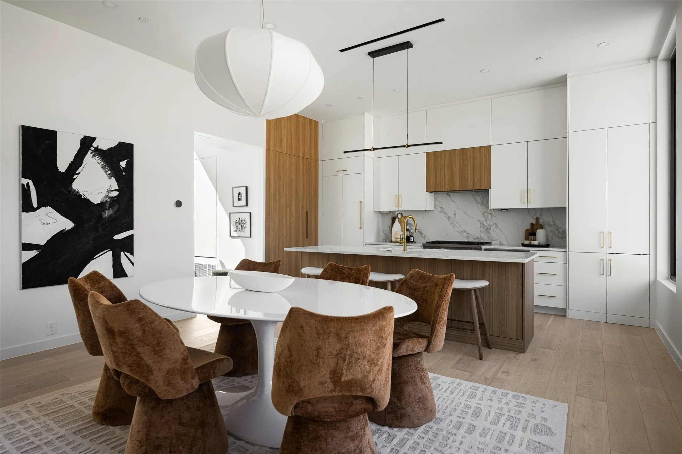 Modern kitchen with white cabinetry and wood-finish accents, large center island with seating, a white countertop, and a marble-finish backsplash