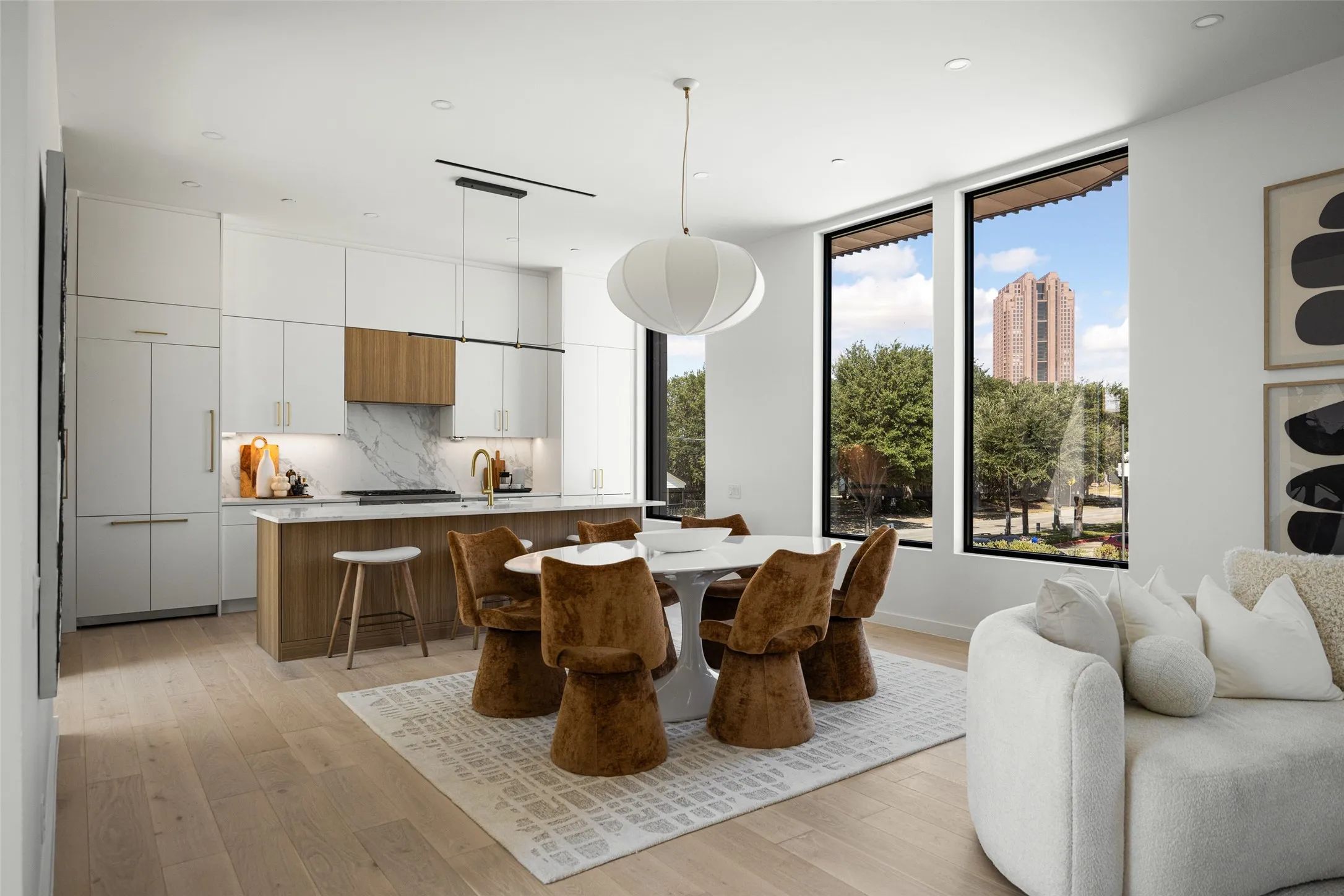 Open-concept living area with wood-finish flooring, a contemporary kitchen featuring integrated appliances, a central island with countertop seating, and expansive windows
