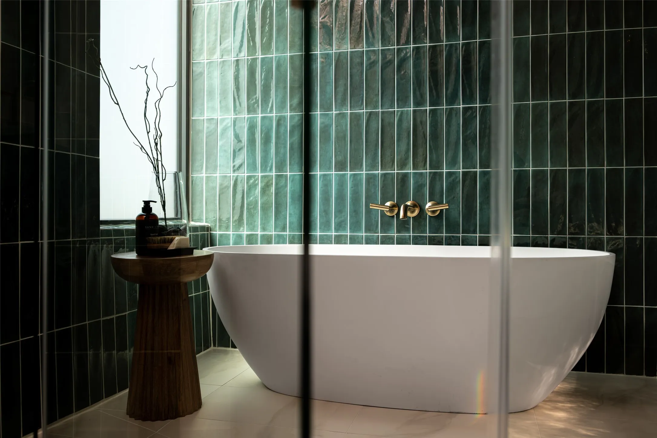Freestanding soaking tub with a wall-mounted brass faucet, set against green subway tile