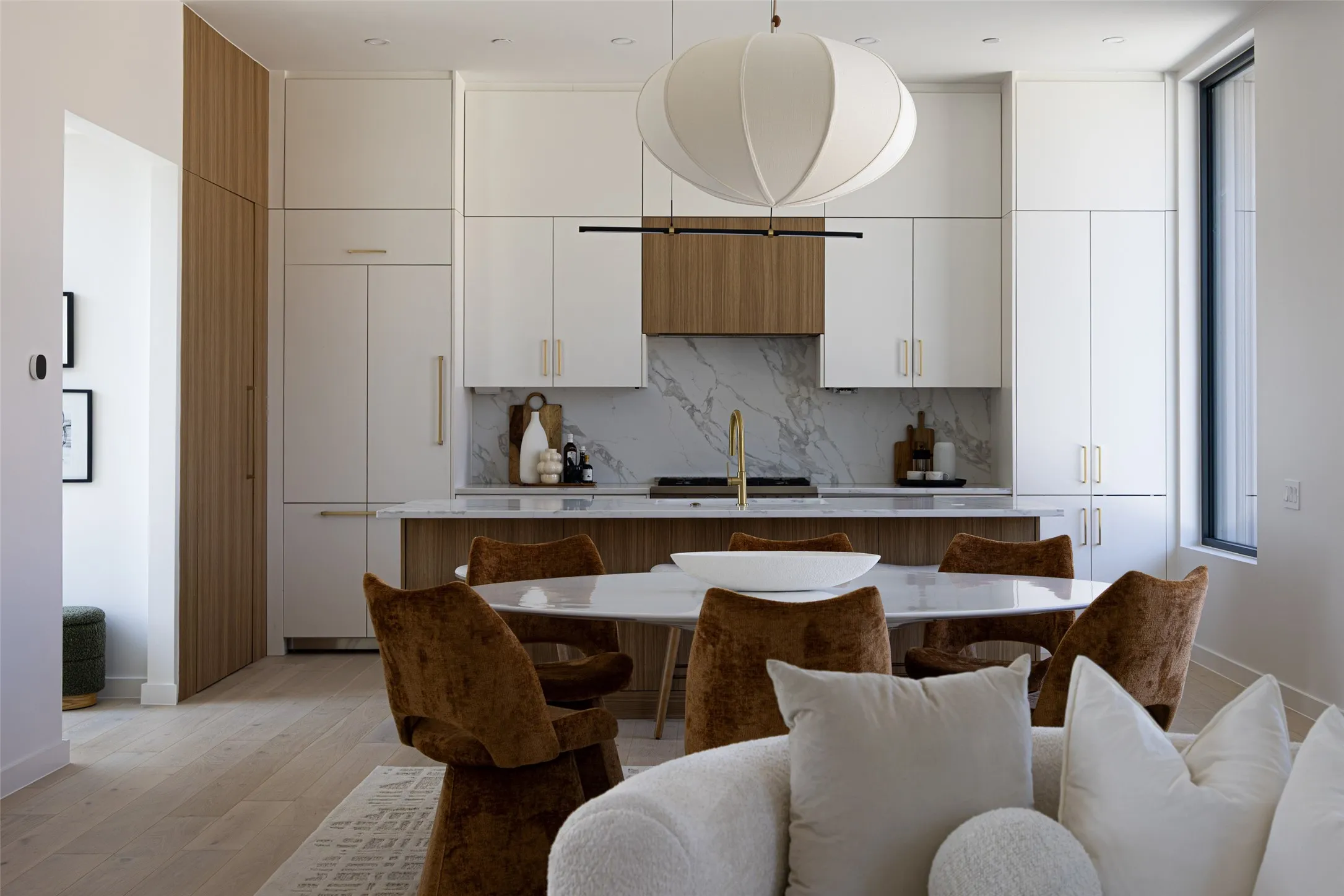 Open-concept kitchen featuring two-tone cabinetry, a full-height marble backsplash, and an integrated refrigerator
