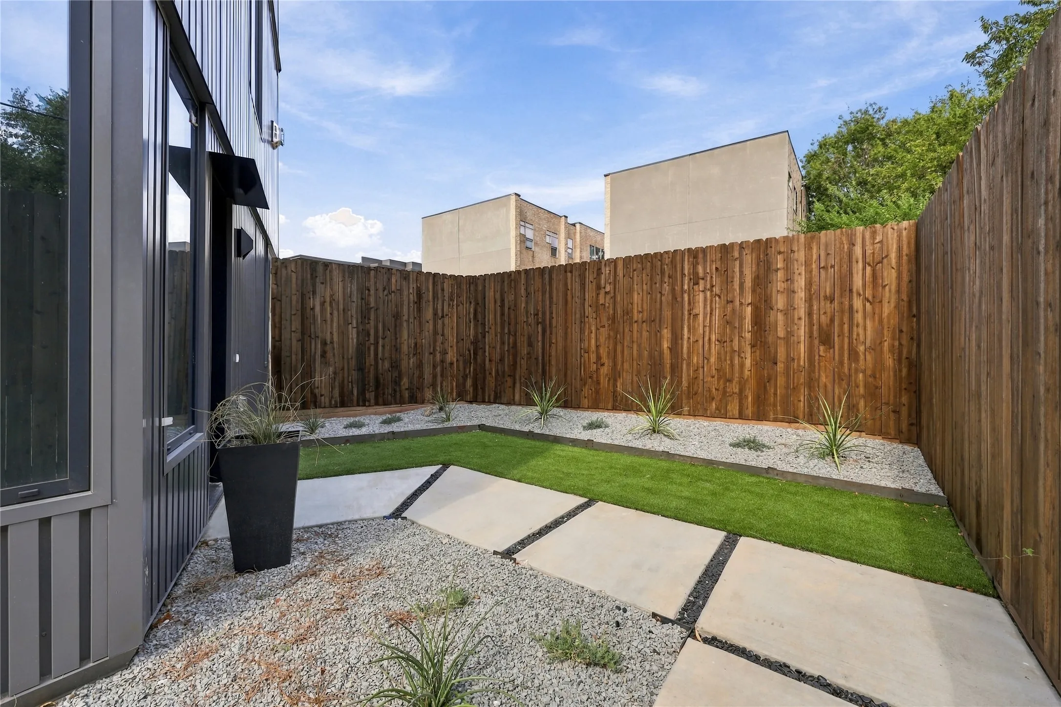 Private fenced yard featuring artificial turf, concrete pavers, and decorative gravel