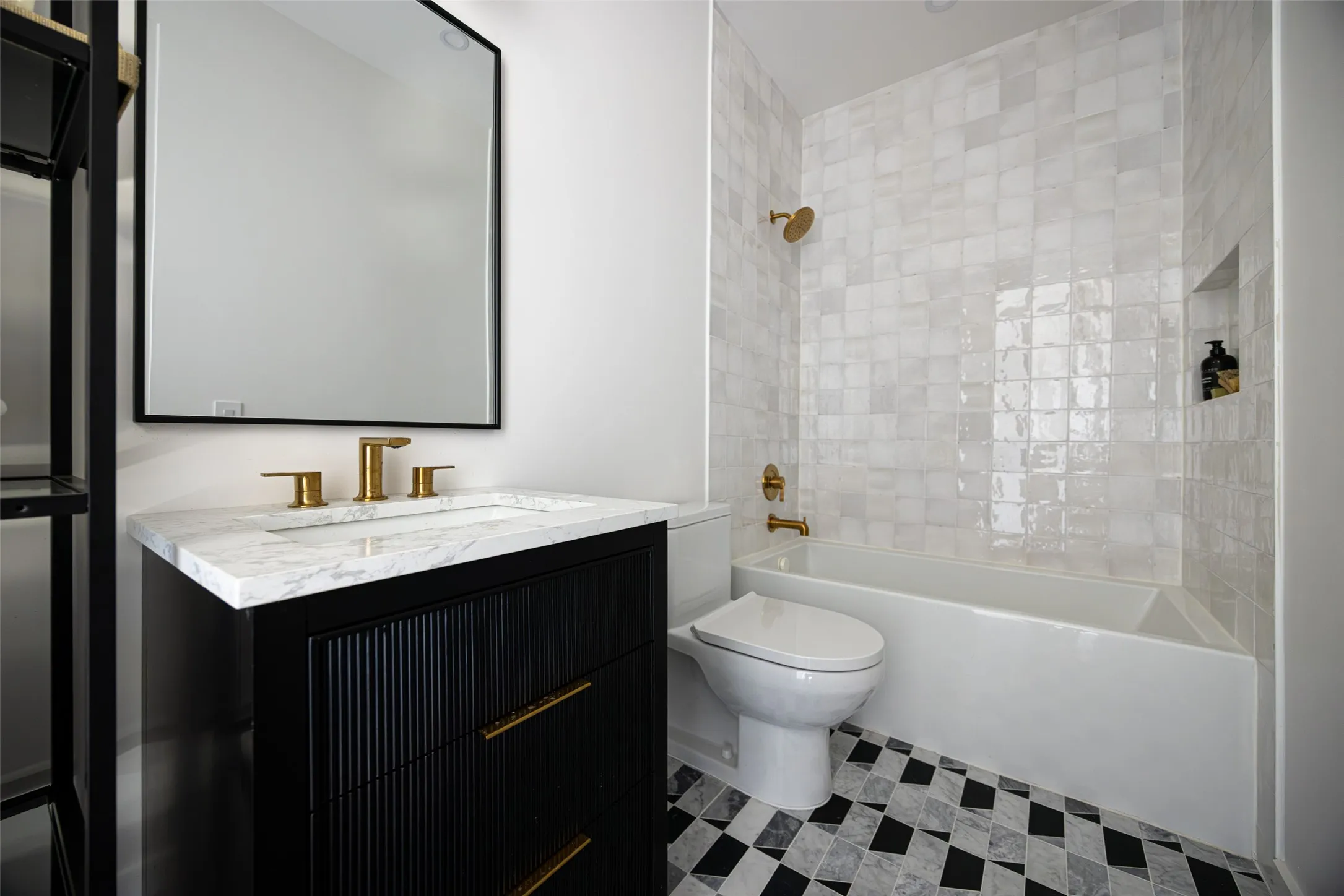 Bathroom featuring a black vanity with gold-tone hardware, a white countertop, a built-in tub with white tile surround, a wall-mounted rectangular mirror, and checkered floor tiling