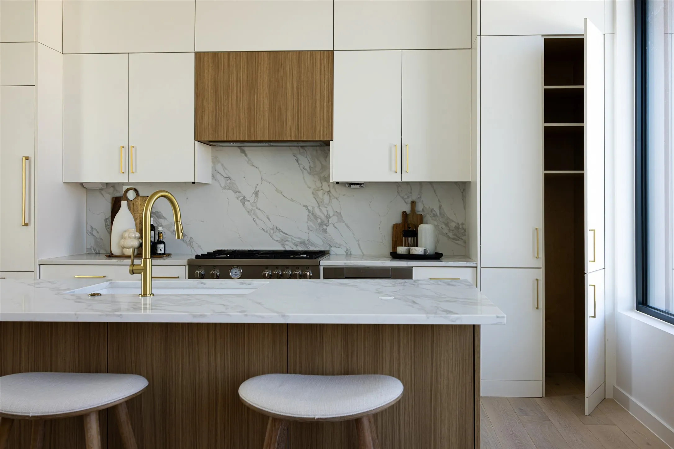 Two-tone cabinetry with gold-finish hardware, integrated paneled refrigerator, marble-patterned backsplash, and a multi-burner range