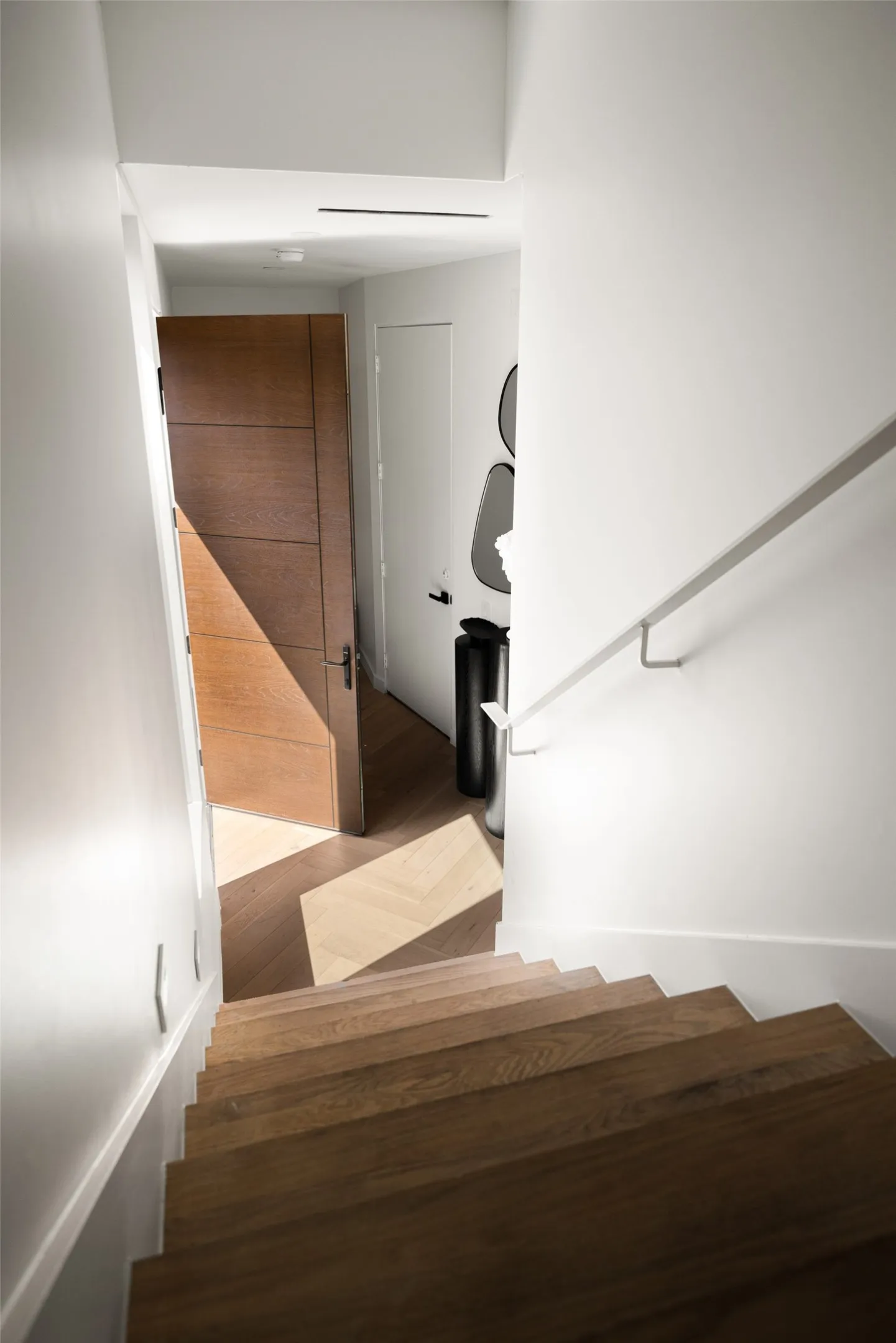 Wood-finish stairway featuring a metal handrail, wood-finish flooring with a herringbone pattern, and a solid wood-finish door