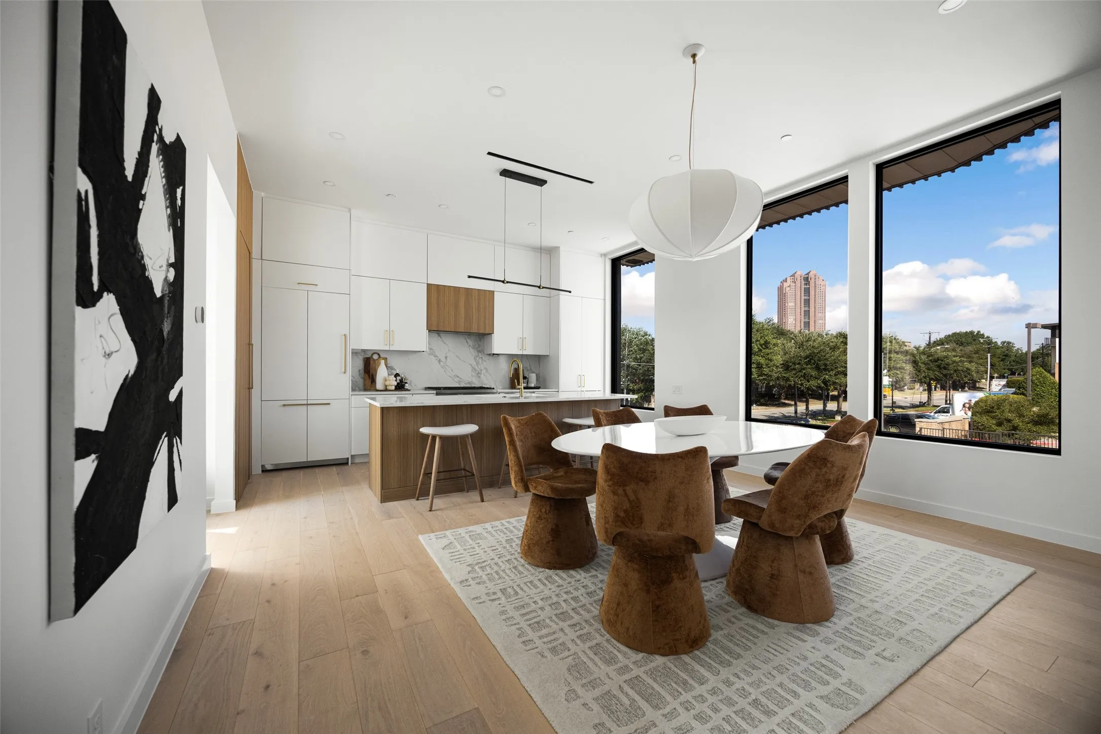 Light wood-finish flooring, recessed lighting, and a modern kitchen featuring white cabinetry, wood-finish island, and an integrated refrigerator