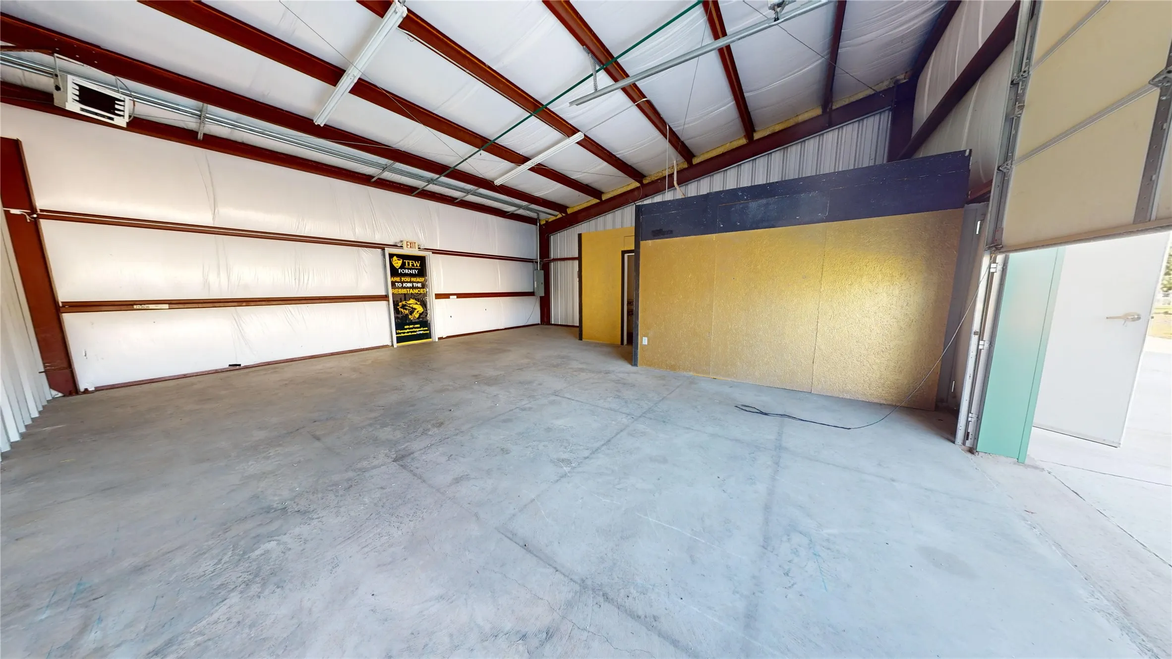 Expansive open-concept space featuring a concrete floor, exposed metal beam ceiling, and a large roll-up door