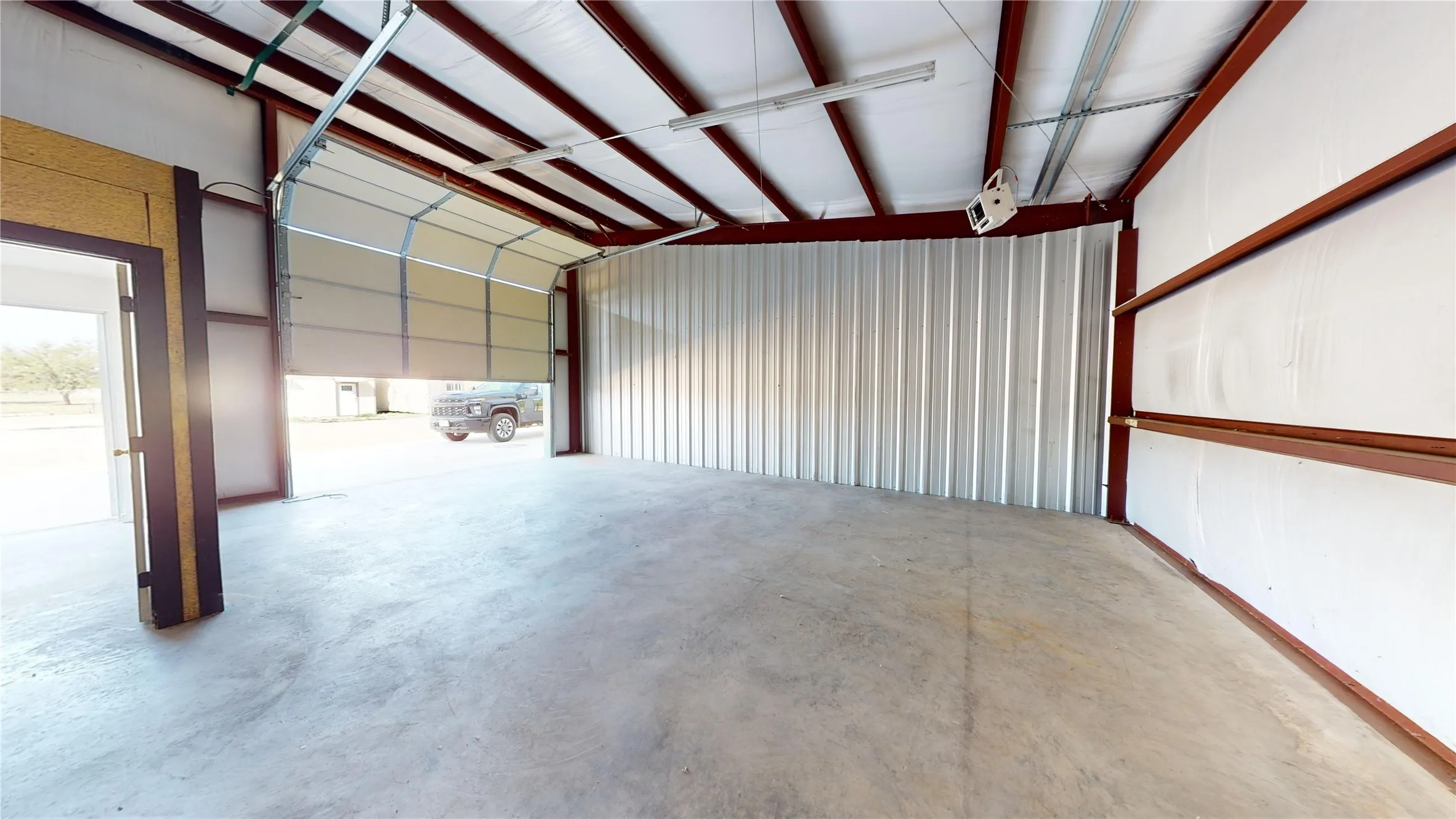 Concrete flooring, insulated walls, exposed metal structural beams, roll-up garage door, and a walk-through entry door