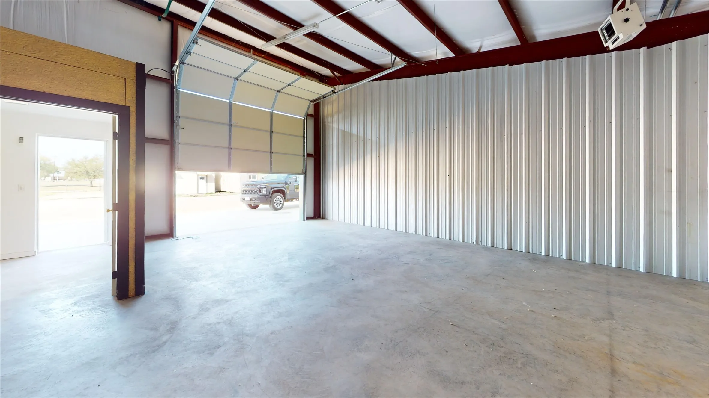 Concrete flooring, metal wall paneling, exposed structural beams, and an overhead roll-up door