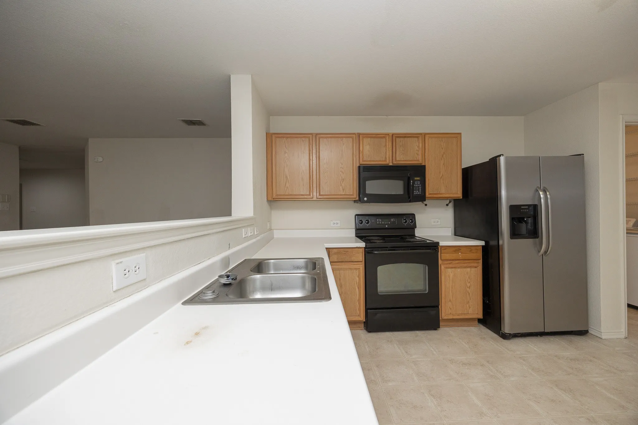 Kitchen featuring wood-finish cabinetry, black appliances, a stainless steel refrigerator, and a double basin sink