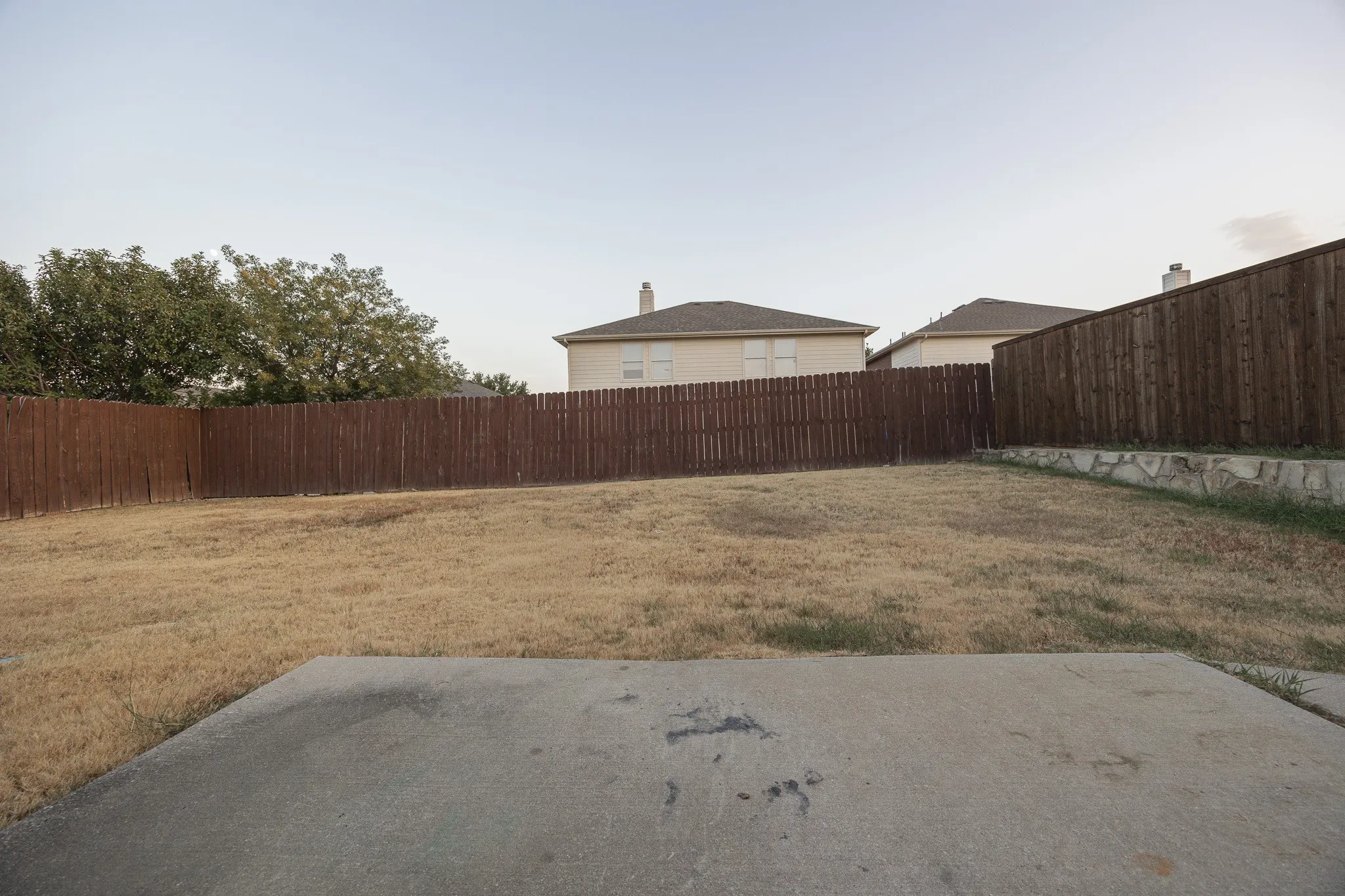 Expansive backyard featuring a concrete patio, wood privacy fencing, and a stone retaining wall
