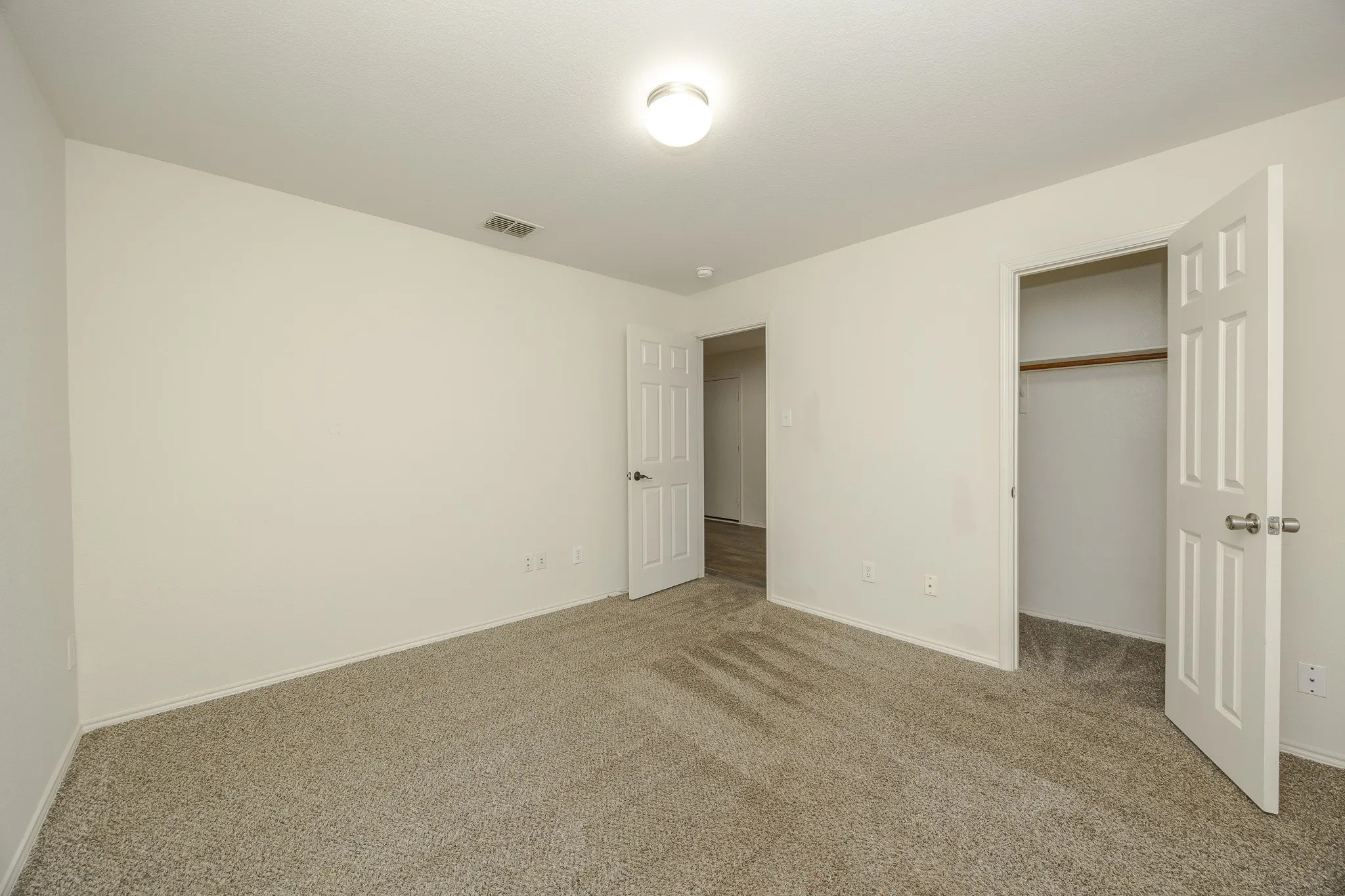 Neutral color palette, plush carpeting, ceiling-mounted light fixture, paneled doors, and closet with hanging rod