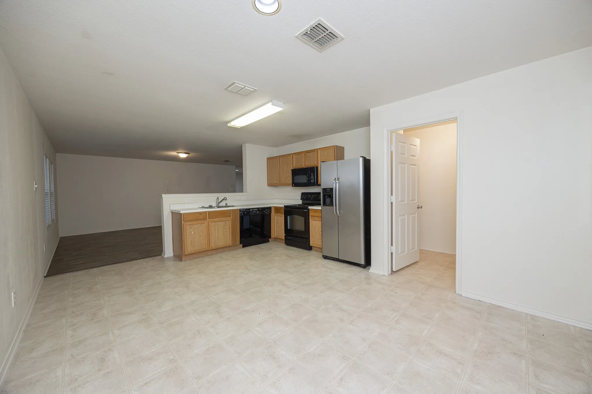 Kitchen featuring wood cabinetry, stainless steel refrigerator, black range, black dishwasher, and a stainless steel sink