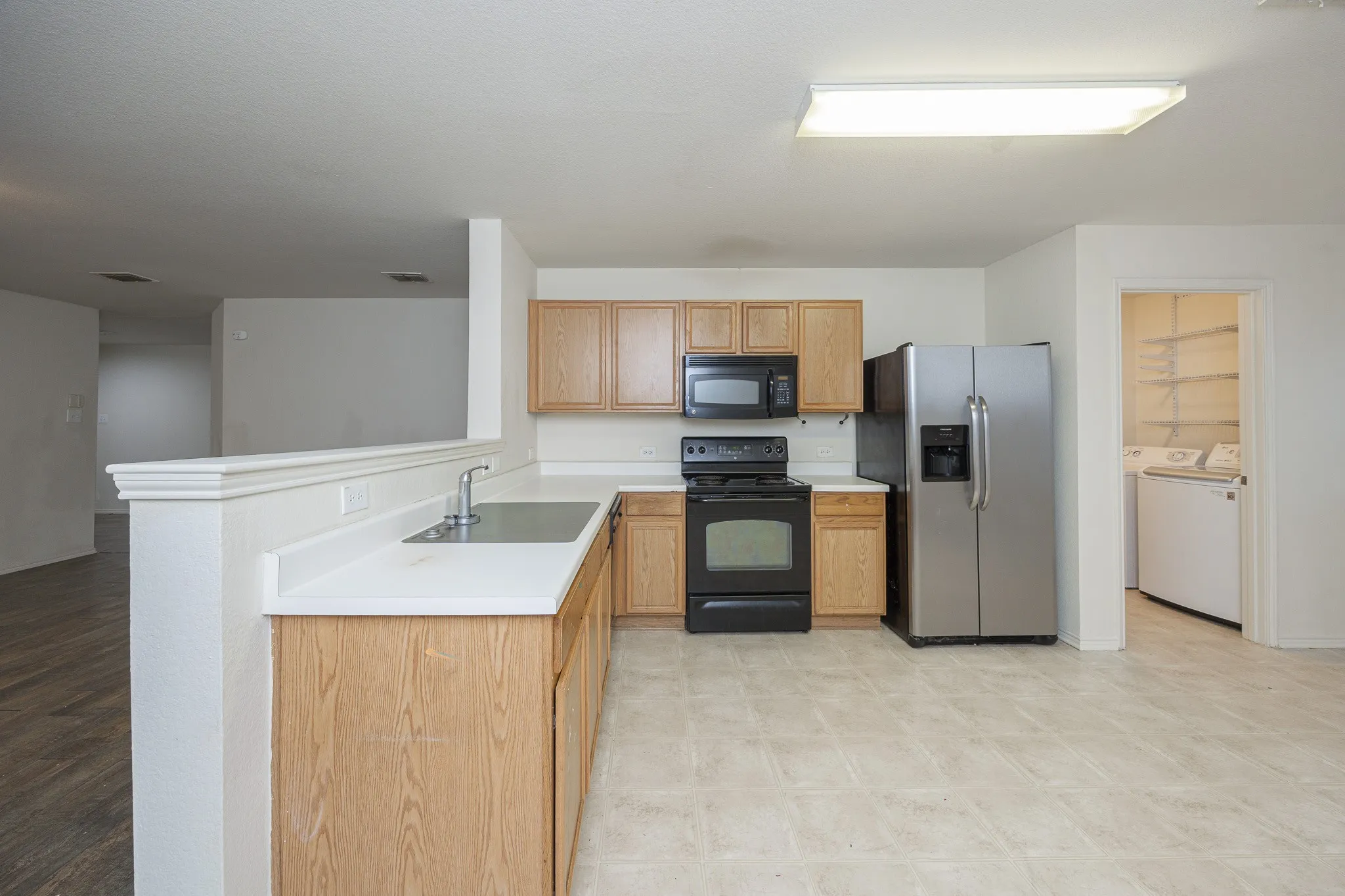 Kitchen featuring wood-finish cabinetry, solid surface countertops, stainless steel refrigerator, and black appliances