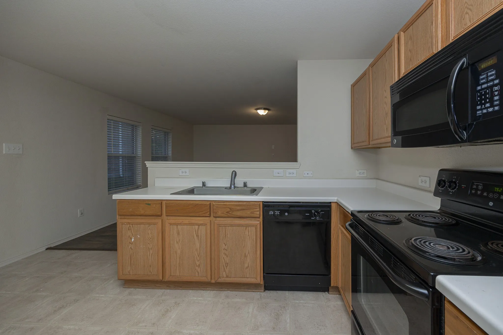 Kitchen featuring wood cabinetry, white countertops, a stainless steel sink, and black appliances
