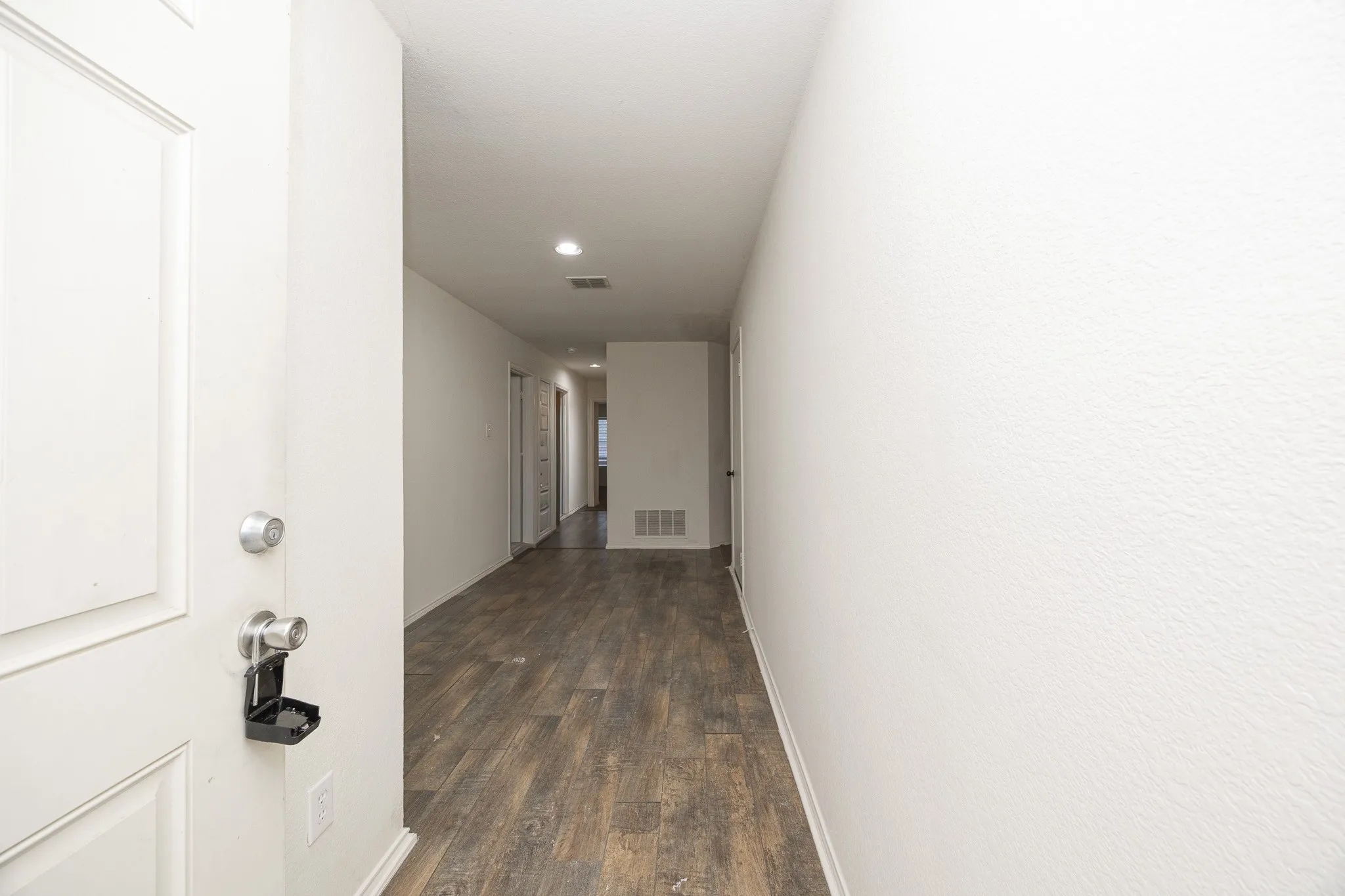 Wood-finish flooring throughout the hallway, recessed lighting, and a white paneled door