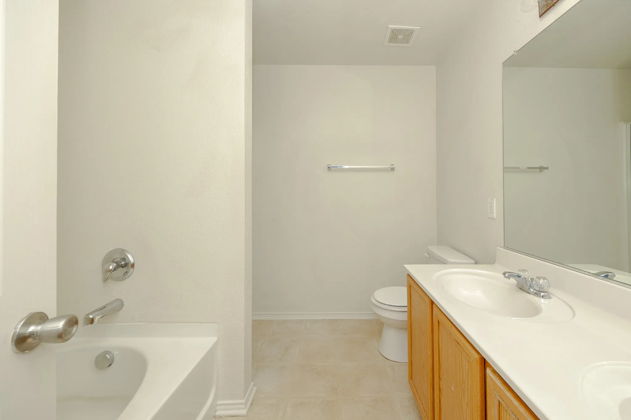 Bathroom featuring a built-in vanity with dual sinks, a large wall-mounted mirror, a built-in bathtub with shower fixtures, and light-toned floor tiling