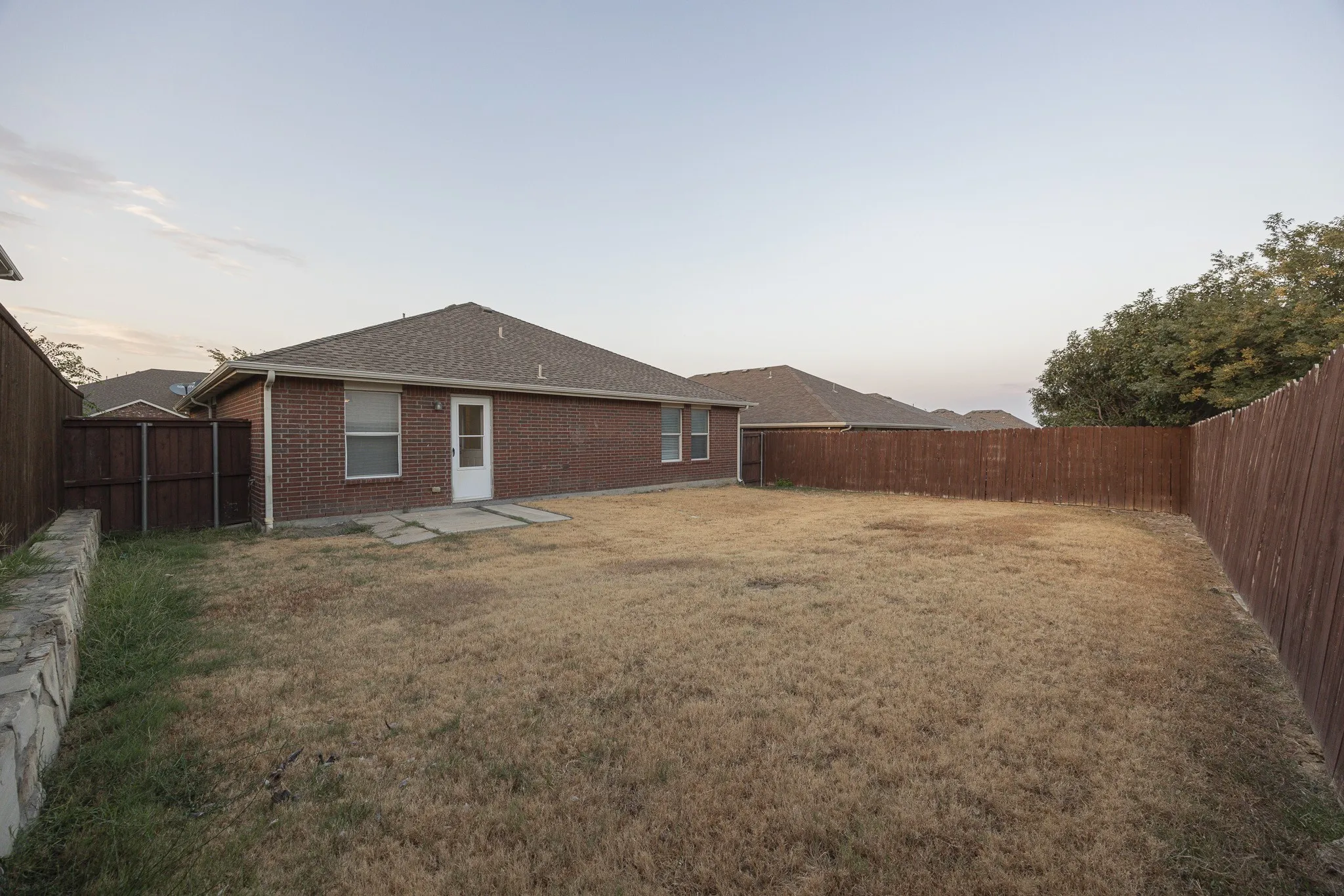 Rear exterior featuring brick siding, a gabled roof, and a privacy fence