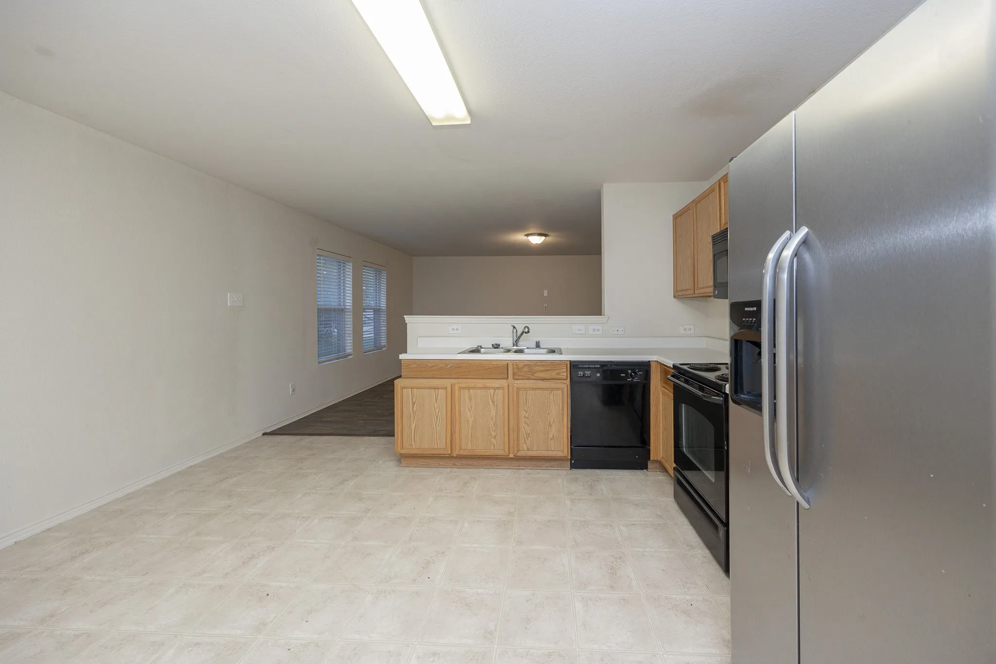 Kitchen featuring light wood cabinetry, a stainless steel refrigerator, and black appliances