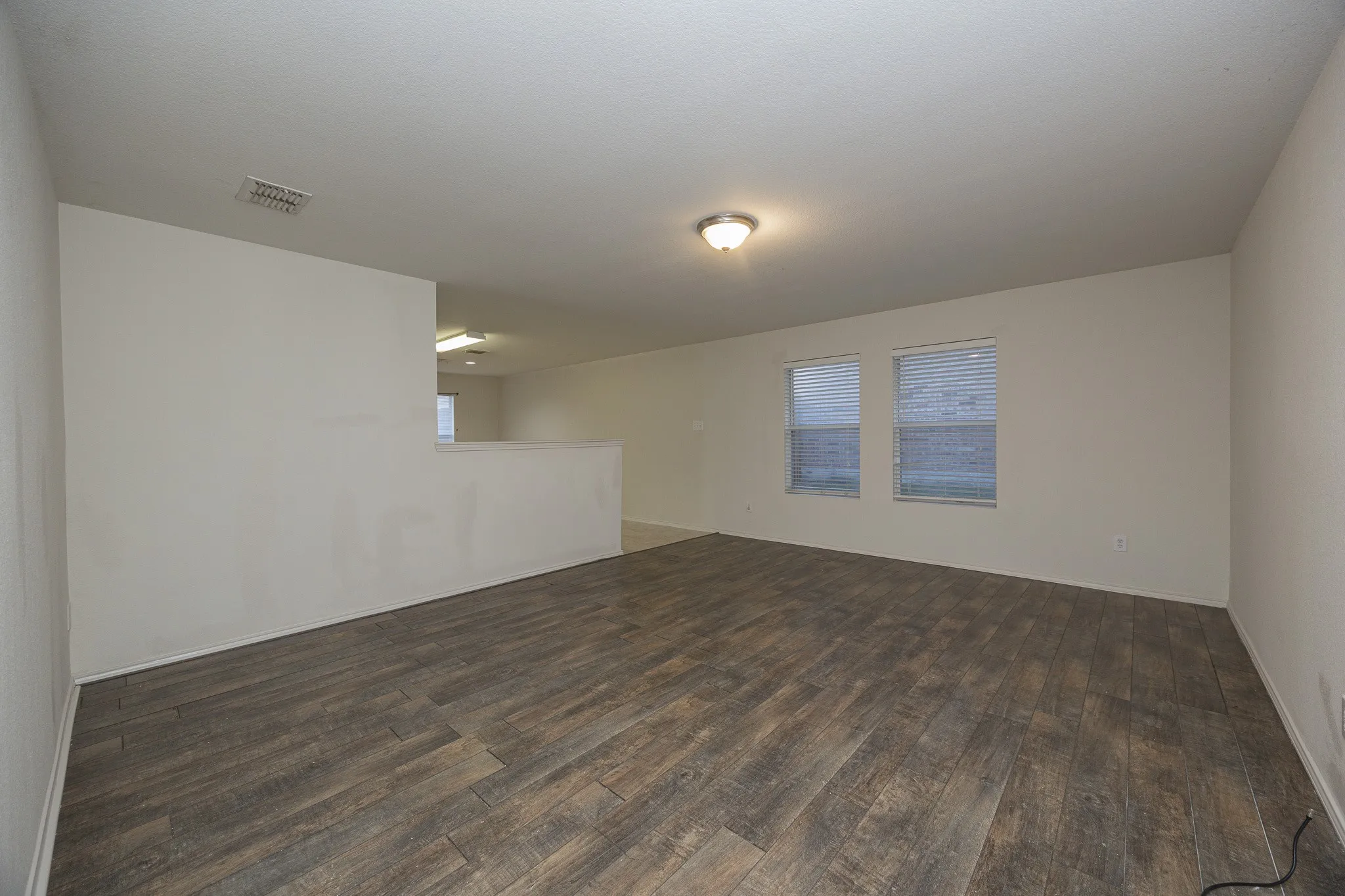 Expansive room featuring wood-finish flooring, two windows with blinds, and neutral wall tones