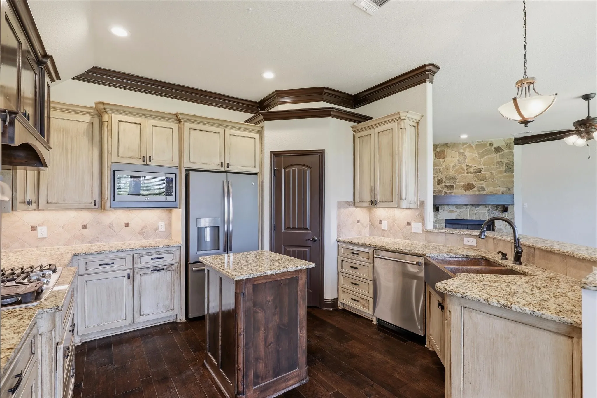 Features include a gas cooktop with a decorative custom hood, stainless appliances, built-in microwave, center island, plentiful cabinetry and drawers, and a distinctive copper-toned farmhouse/apron-front sink.