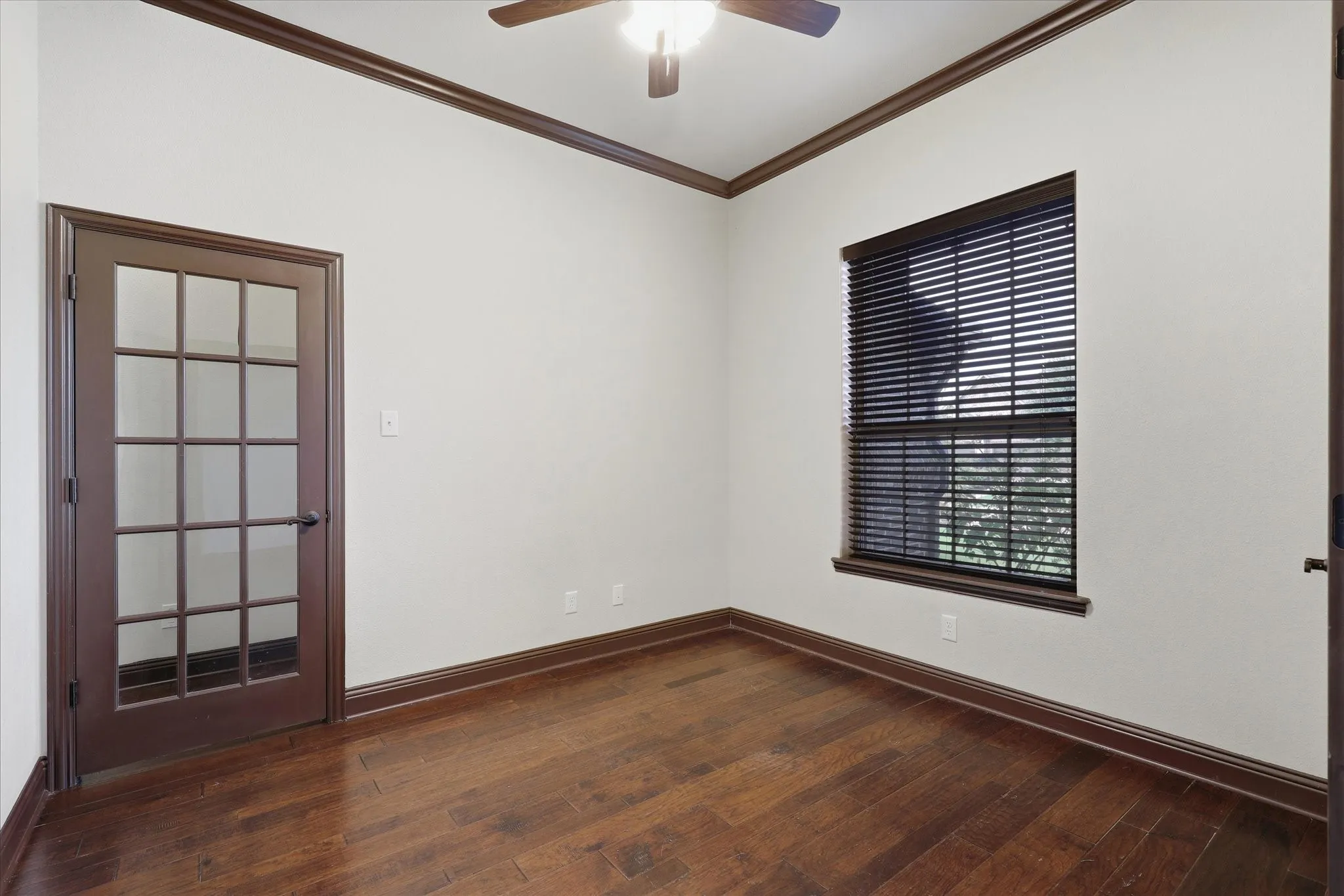 Dedicated office with hardwood flooring, substantial crown molding and baseboards, a large window and French door.