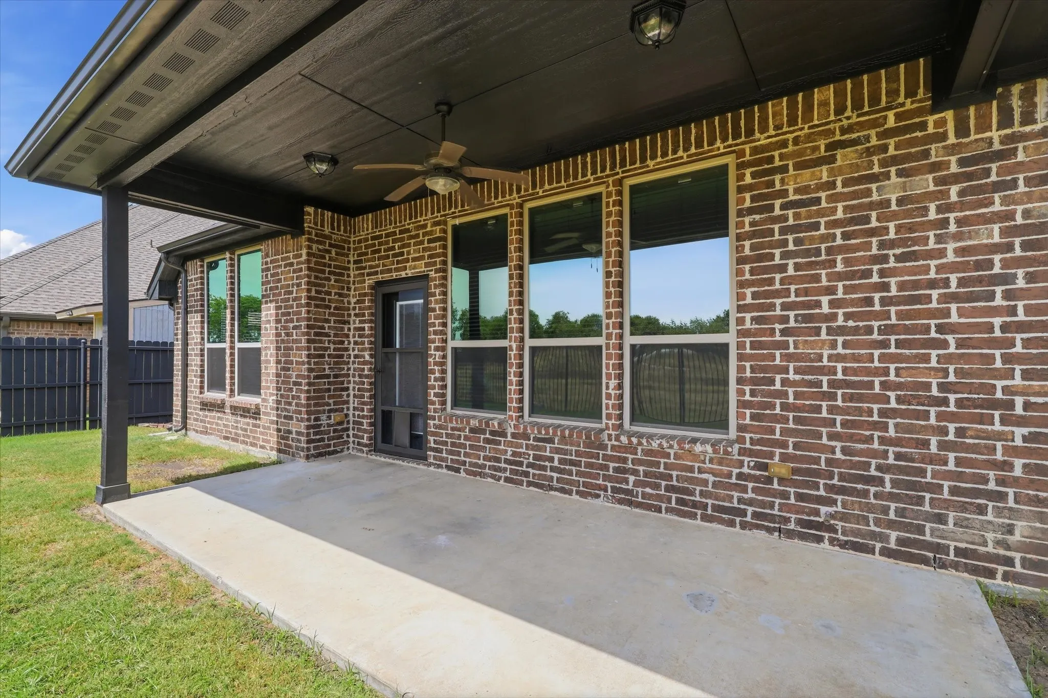 Generously sized covered back patio extends the living space outdoors. It includes a ceiling fan and exterior lighting, with plenty of room for a dining set, seating area or grill setup.