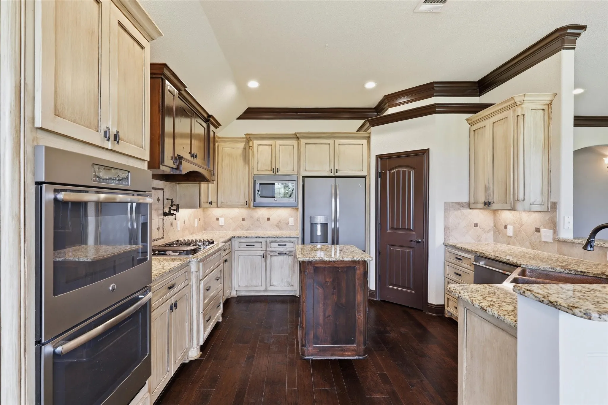 Distressed light-finish cabinetry contrasted by dark-stained accent cabinetry and island, granite countertops and an extensive tile backsplash.