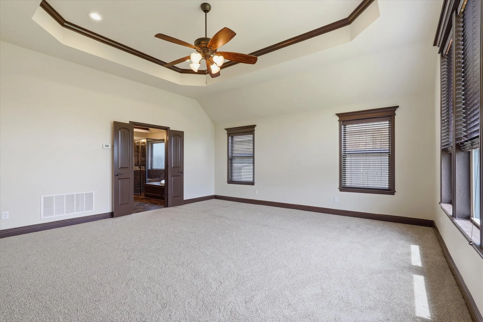 Spacious primary suite with a large tray ceiling accented by dark-stained crown molding, double doors provide a grand entrance into the primary bath.