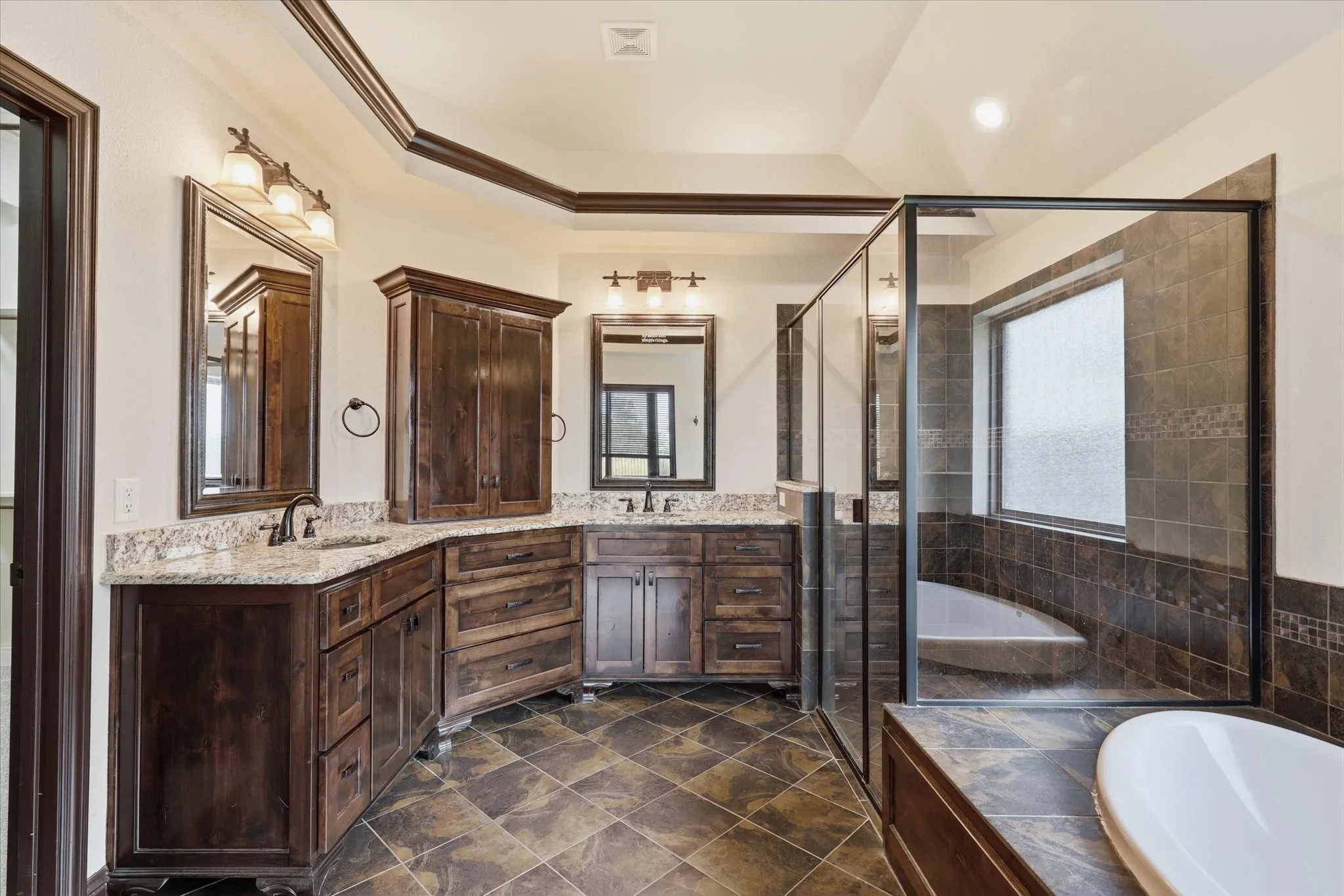 Generously sized bath with extensive custom wood cabinetry and granite countertops, separate vanity areas, large mirrors and decorative lighting.