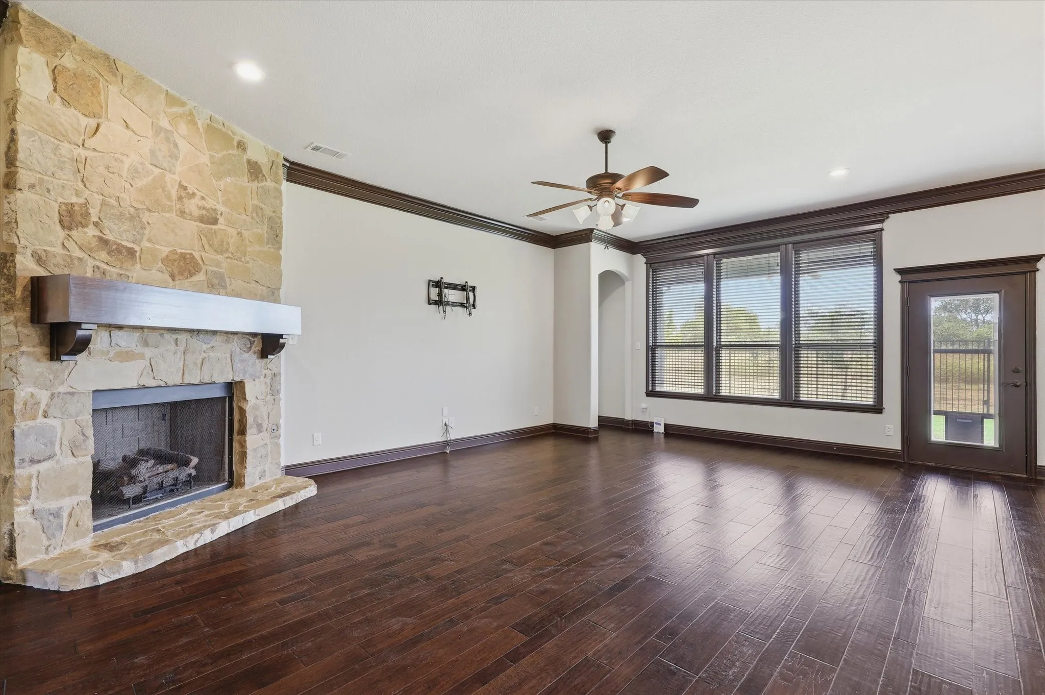 Spacious living area featuring rich hardwood floors and an impressive floor-to-ceiling natural-stone fireplace with a substantial wood mantel.