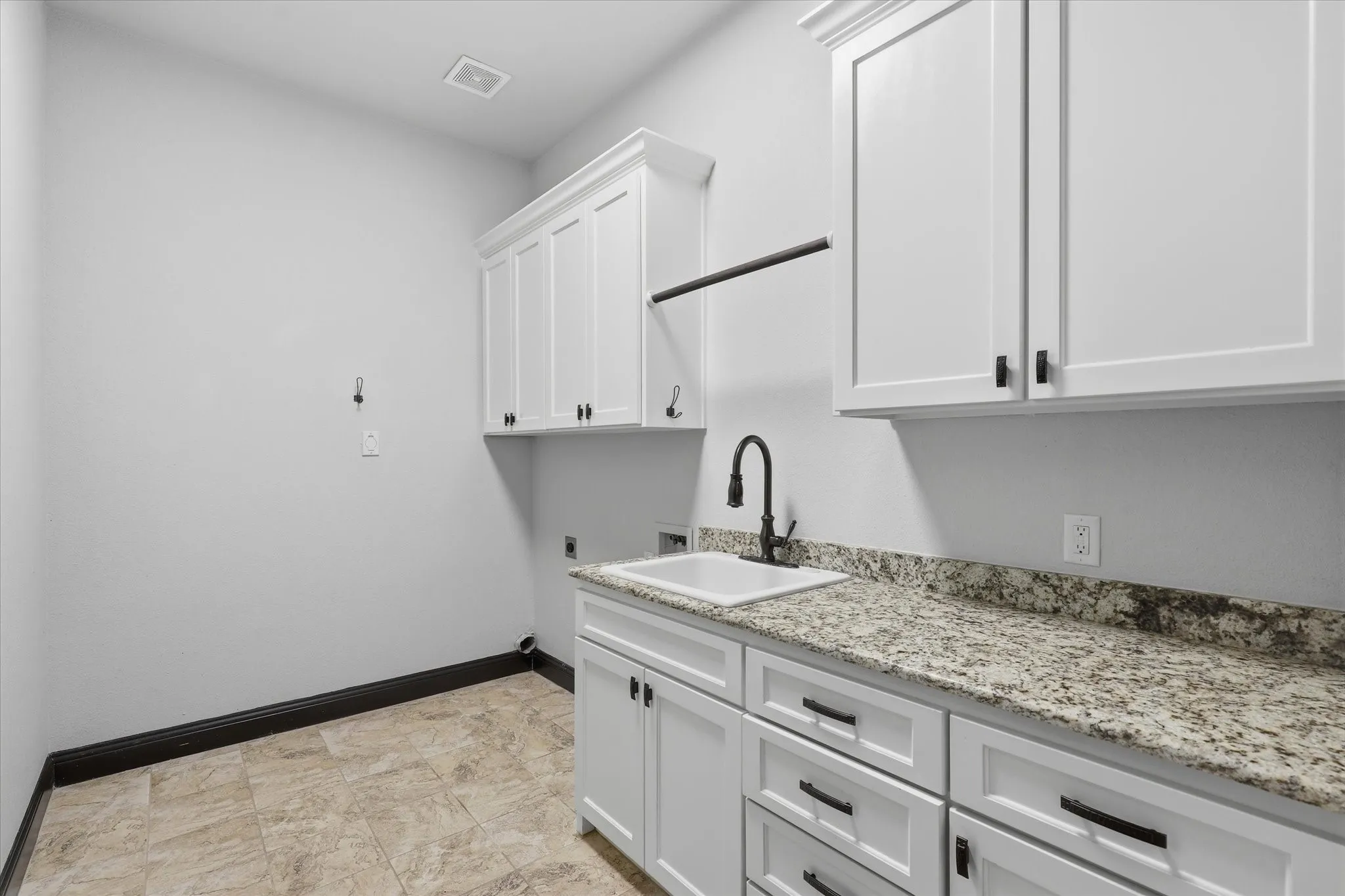 A very functional utility room with granite countertops, utility sink, abundant upper and lower cabinetry, hanging rod and additional counter/work space.