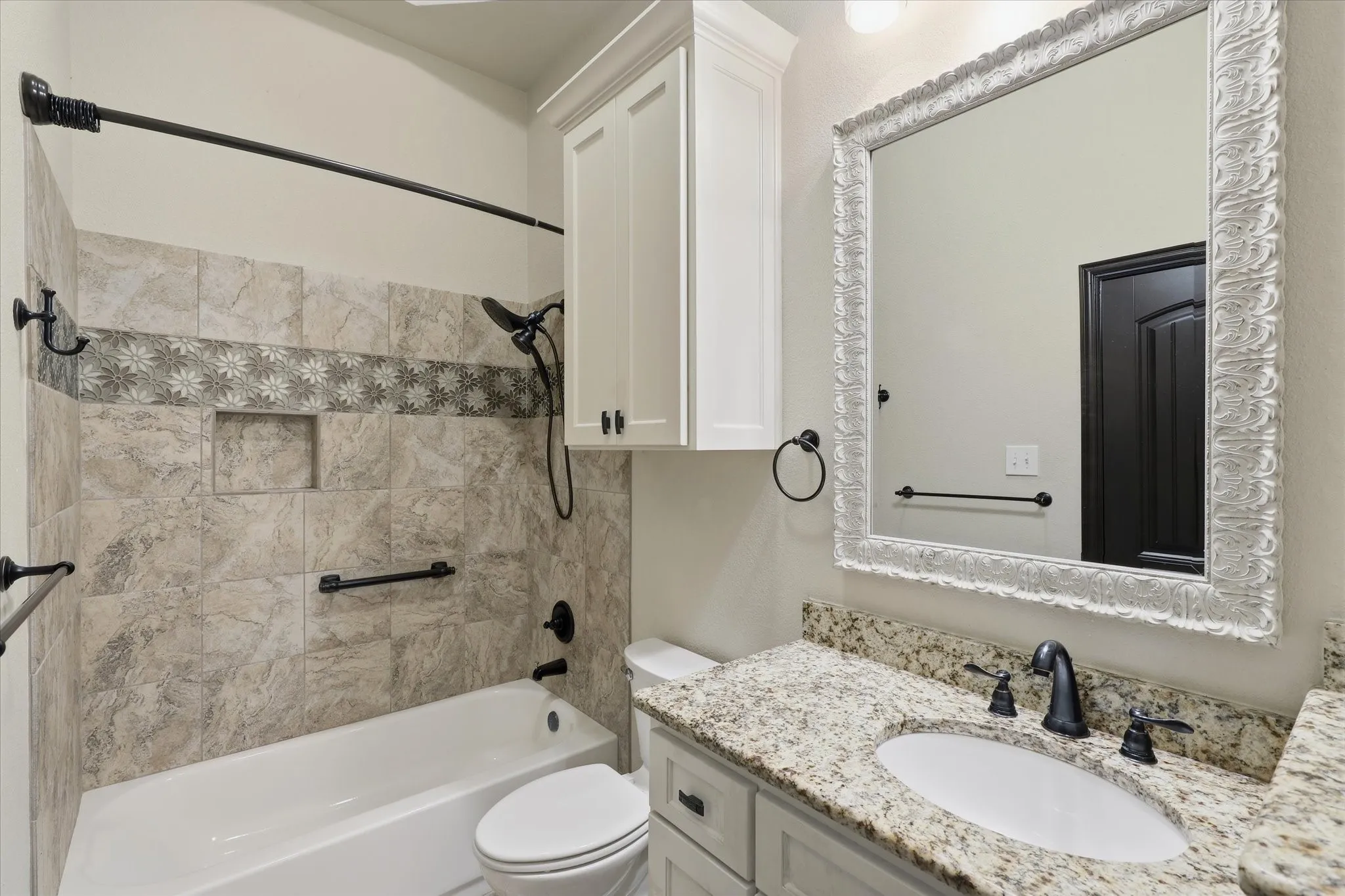 Tub/Shower combination features an extensive tile surround with a decorative mosaic accent band, built-in shower niche and coordinating dark fixtures. A custom cabinet above the toilet provides additional storage.