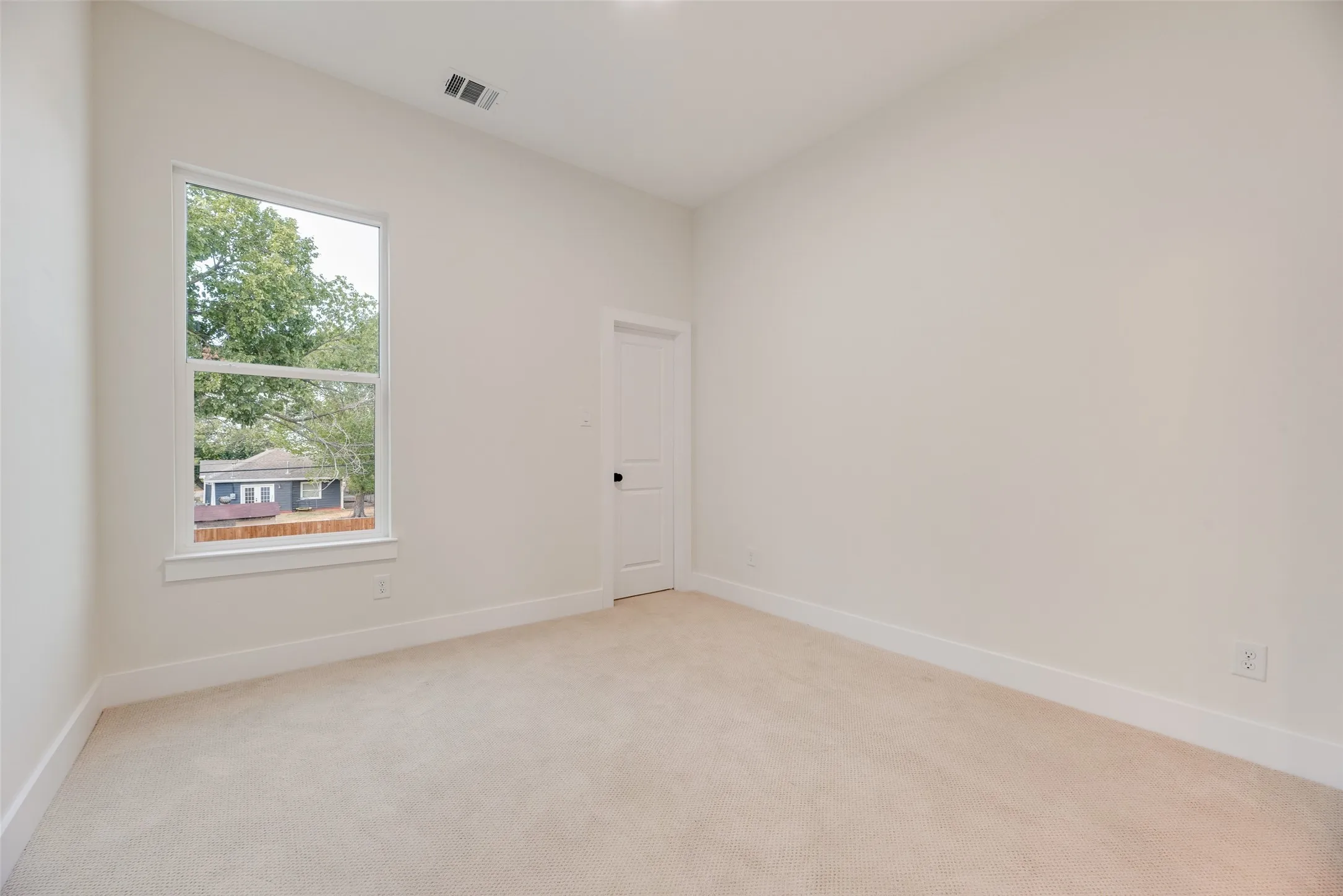 Neutral wall paint finish, plush carpeting, white trim, single window, and a paneled interior door