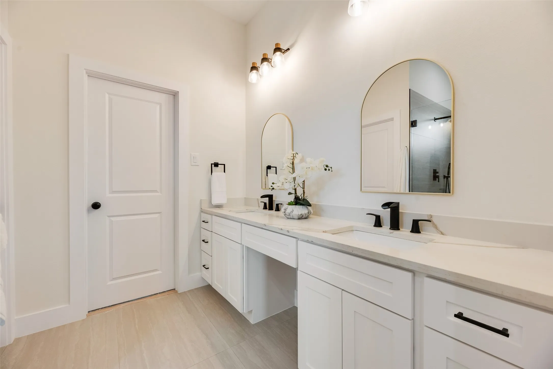 Dual vanity with white cabinetry, integrated sinks, black fixtures, and arched mirrors