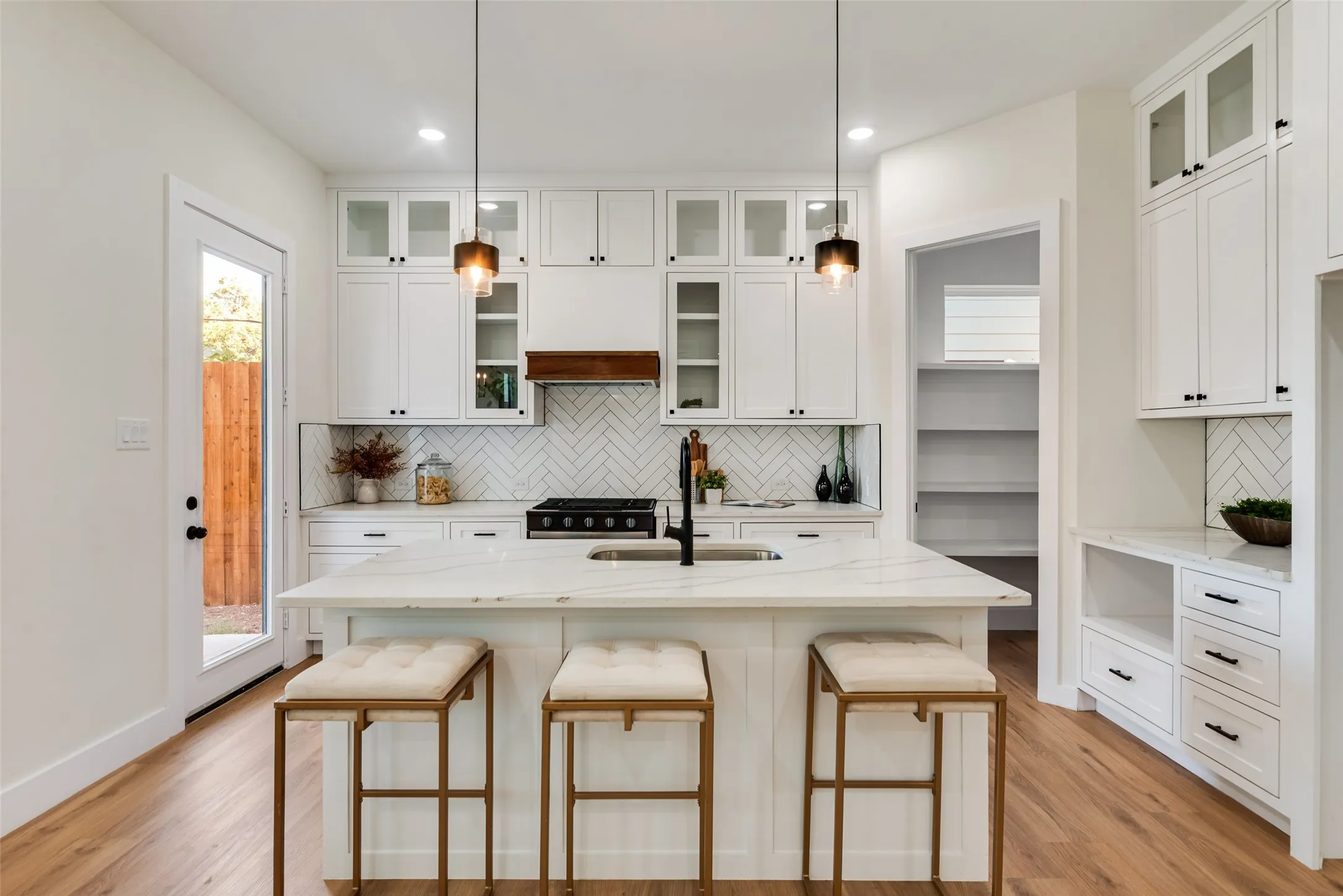 Kitchen featuring white cabinetry, a large center island with a sink, wood-finish flooring, a herringbone tile backsplash, and a built-in pantry