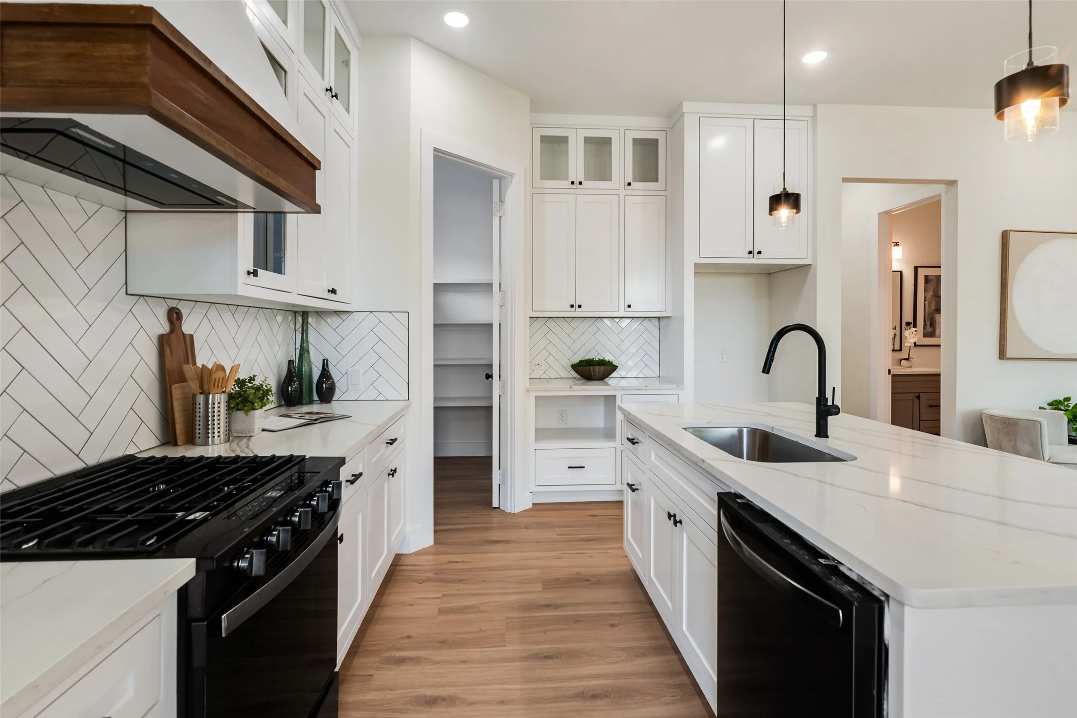 White shaker cabinetry, wood-finish flooring, white countertops, herringbone tile backsplash, and a built-in pantry