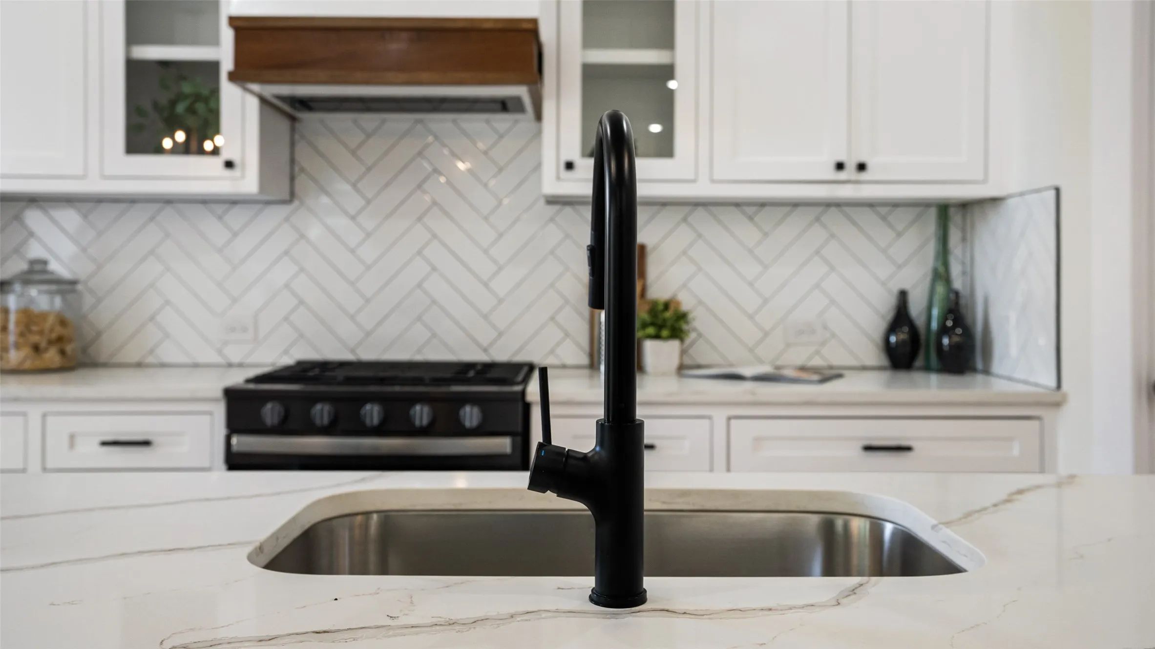 Kitchen featuring a stainless steel sink with a matte black faucet, white shaker-style cabinetry, a herringbone tile backsplash, and a built-in gas range
