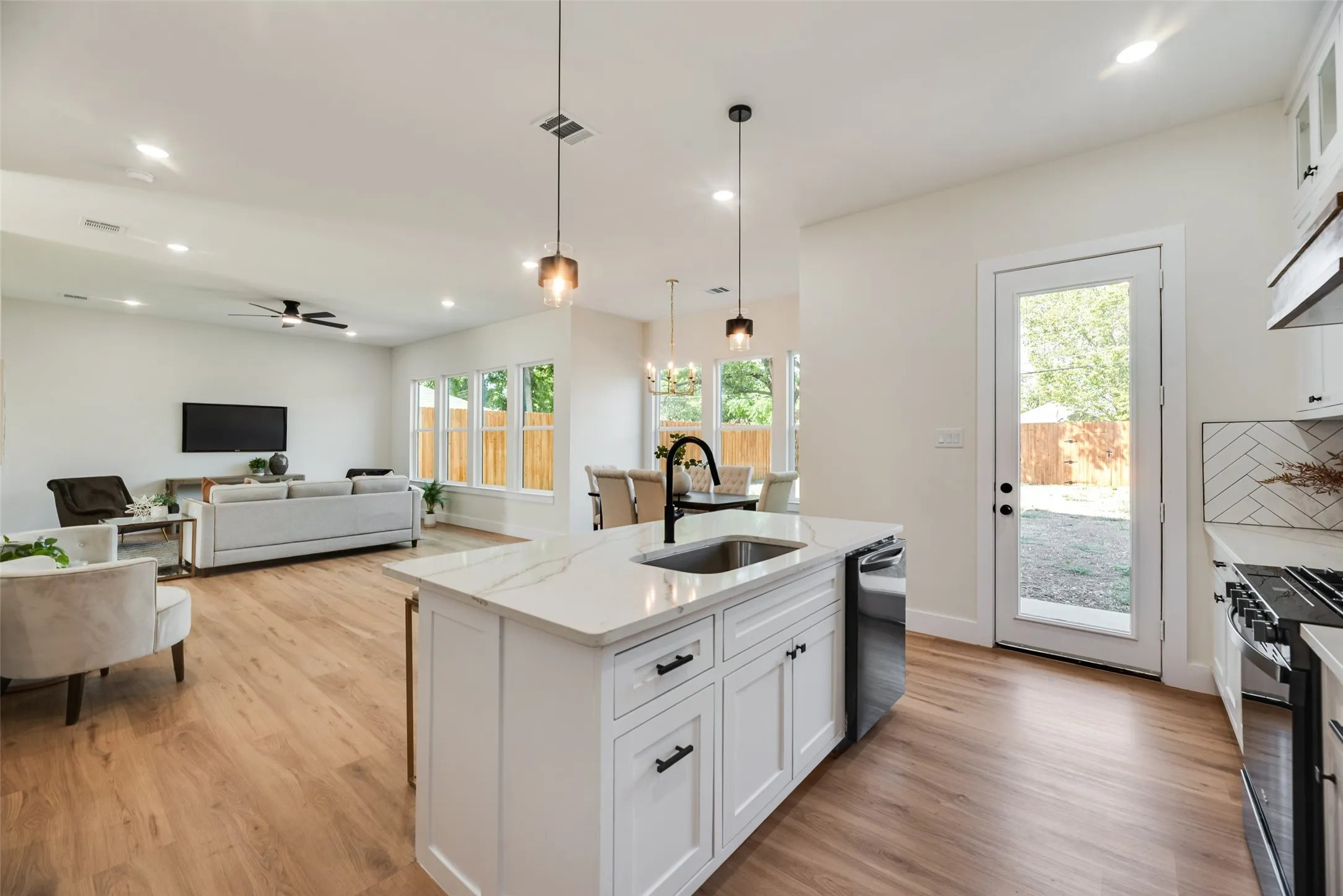Kitchen island with a white countertop and integrated sink, pendant lighting, wood-finish flooring, white cabinetry, and a glass-paneled door