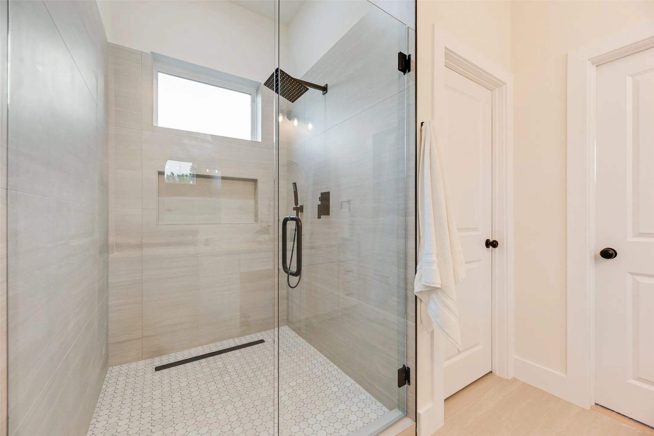Glass-enclosed shower with a rainfall showerhead, tiled walls, hexagonal floor tiling, and a recessed niche